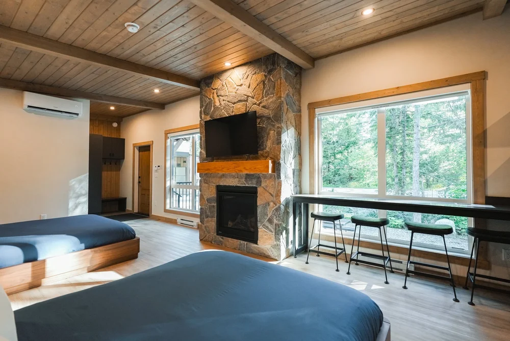 Inside a Selkirk cabin: two queen beds facing a stone gas fireplace