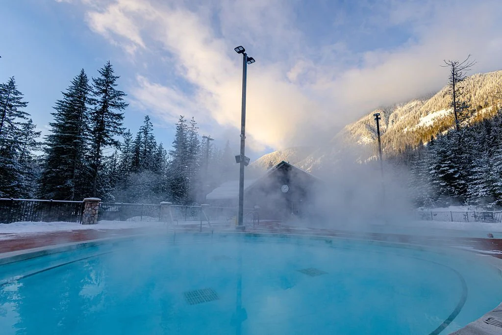 Steam rising off a Crazy Creek hot pool surrounded by snowy trees and mountains