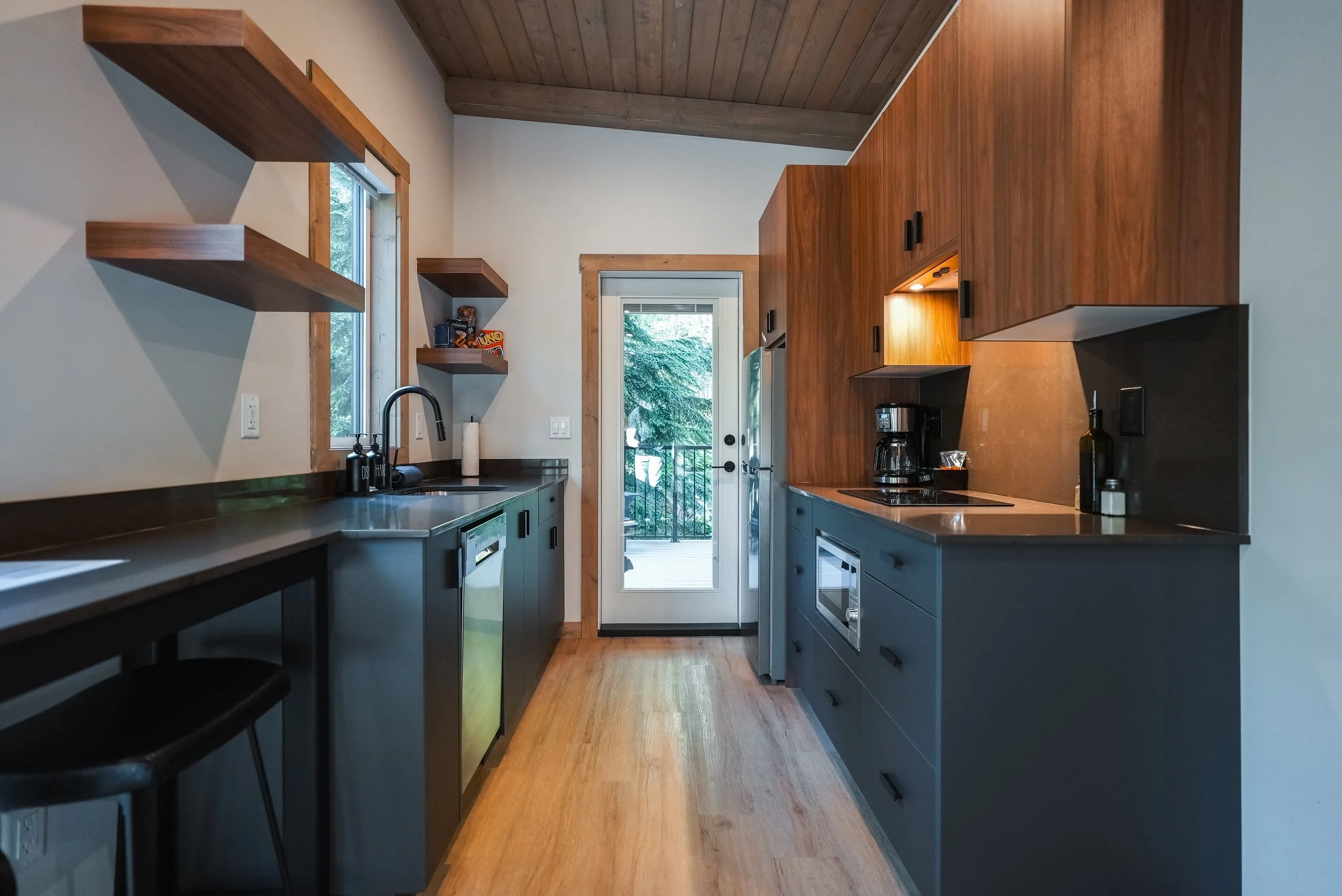 Selkirk kitchen with dark cabinets, open wood shelves and a door to the deck