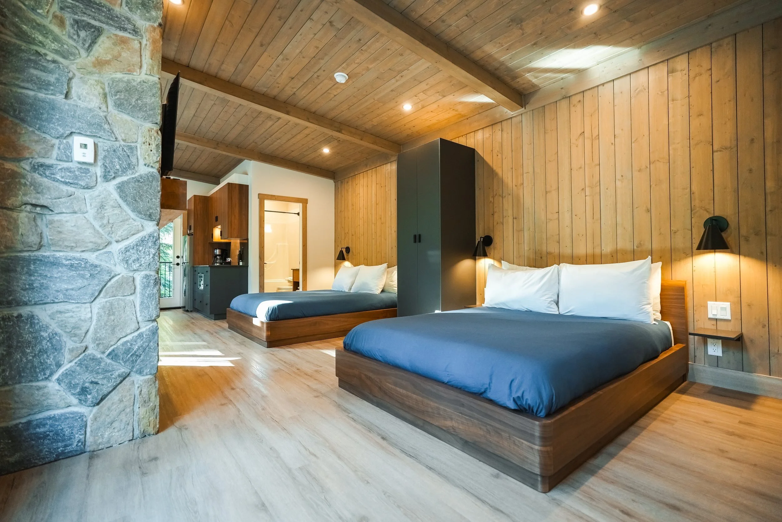 Two queen beds in the Selkirk beside a stone accent wall