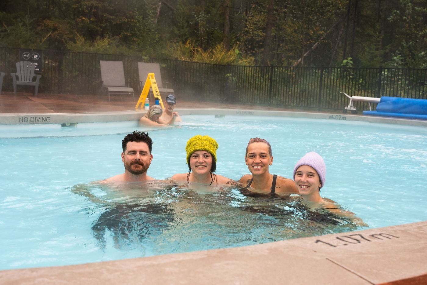 Four friends in colourful toques soaking together in a steaming pool in the fall
