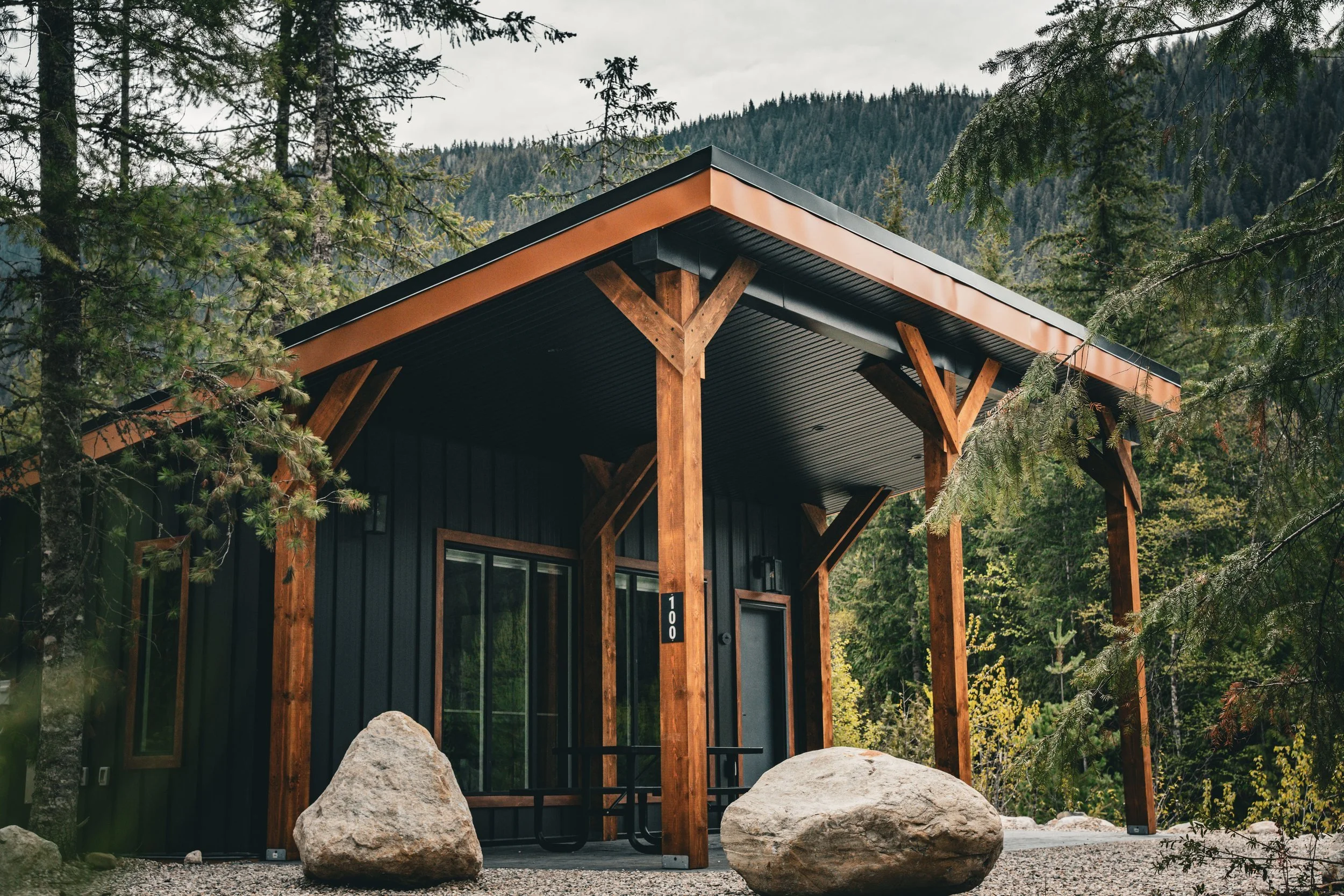 Monashee cabin with a timber-framed covered deck, surrounded by forest and large boulders