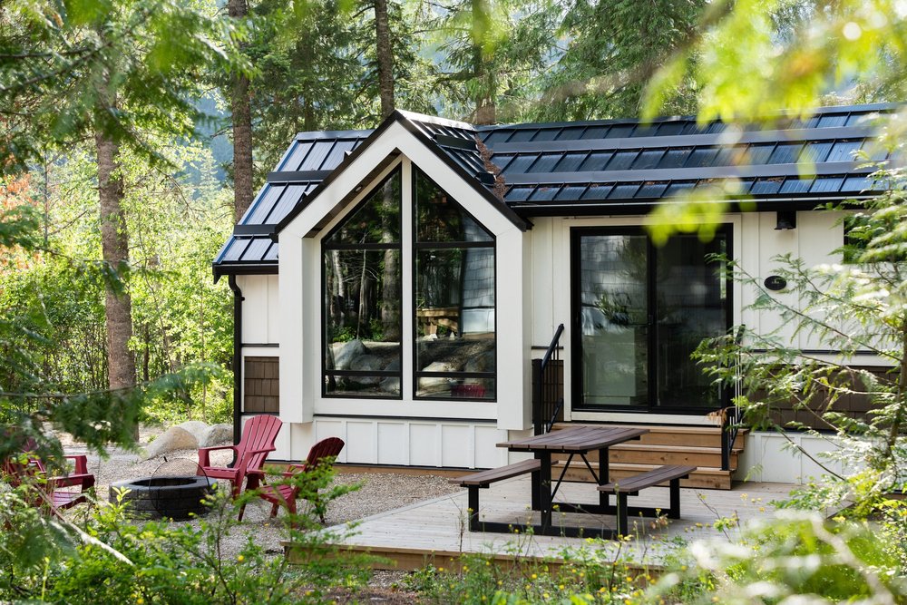 The Apex cabin with its tall gabled window wall and red Adirondack chairs among the trees