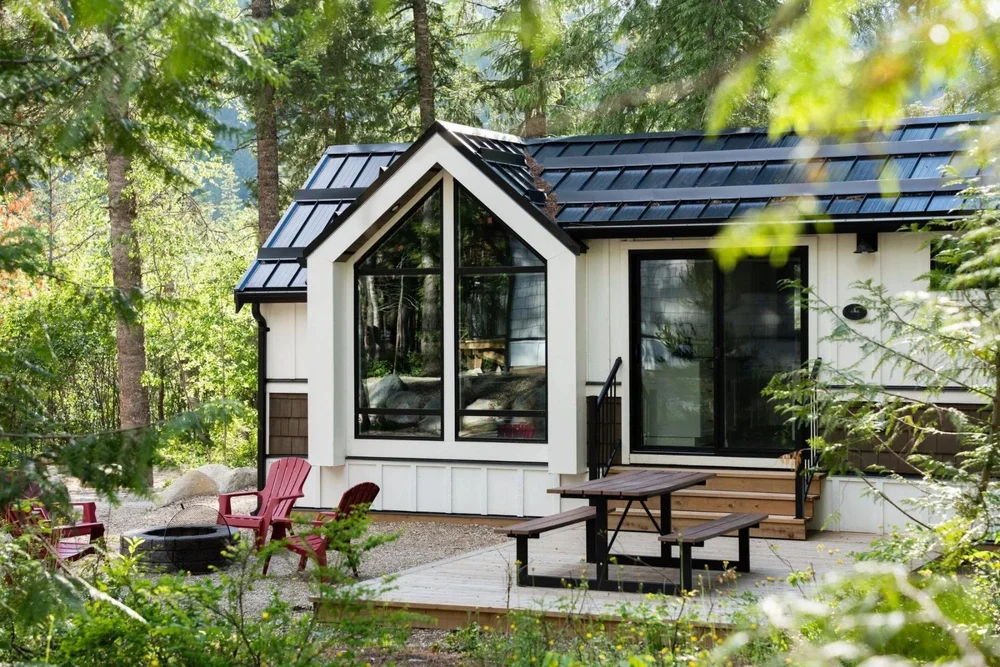 The Apex cabin with its tall gabled window wall and red Adirondack chairs among the trees