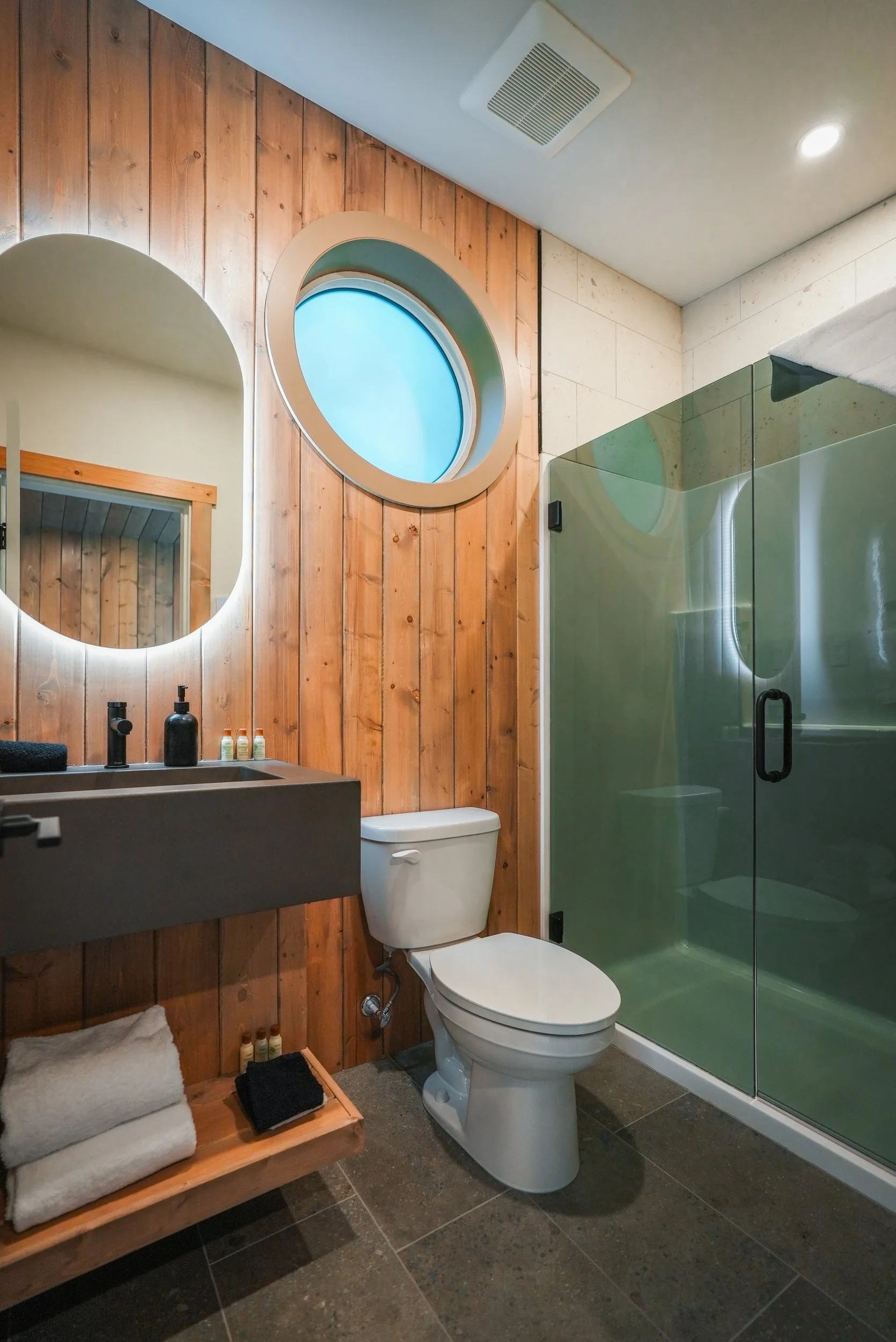 Nest bathroom with a round mirror, a porthole window and a glass shower