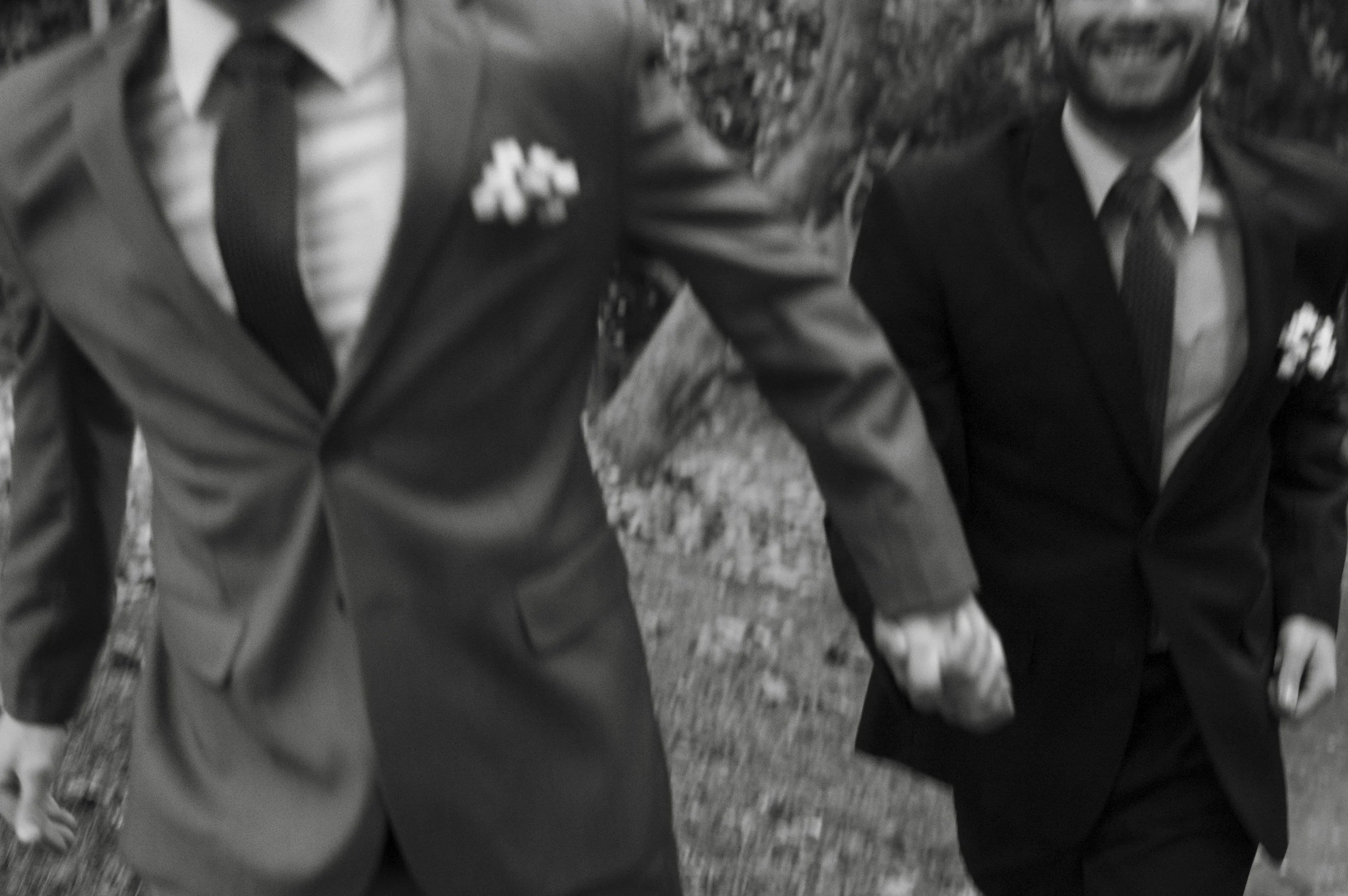 A black and white close-up of two men in suits holding hands, representing that marriage therapy is not a courtroom or blame session