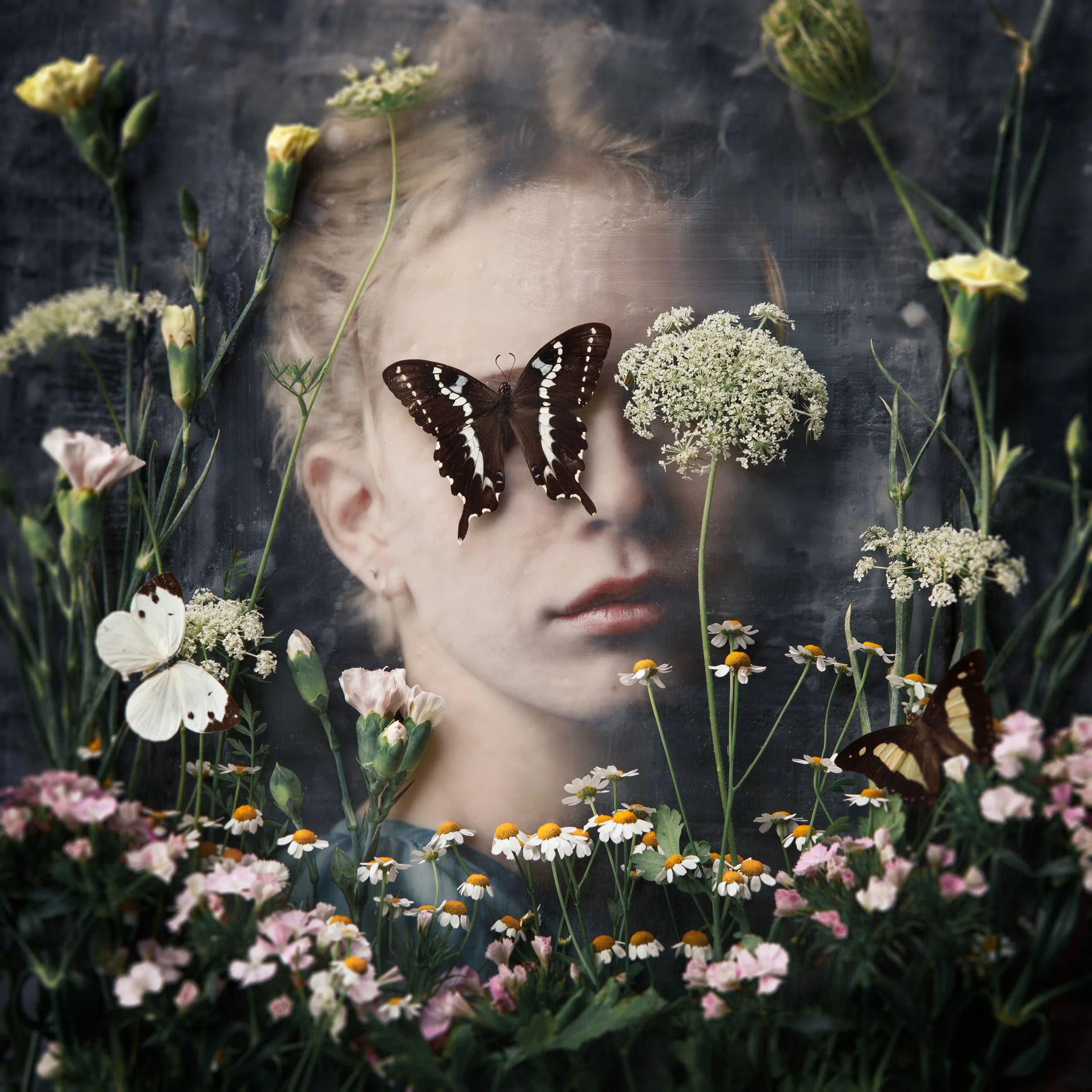 A woman's face behind a foggy glass surrounded by various white, yellow, and pink flowers with butterflies on the glass and among the flowers.