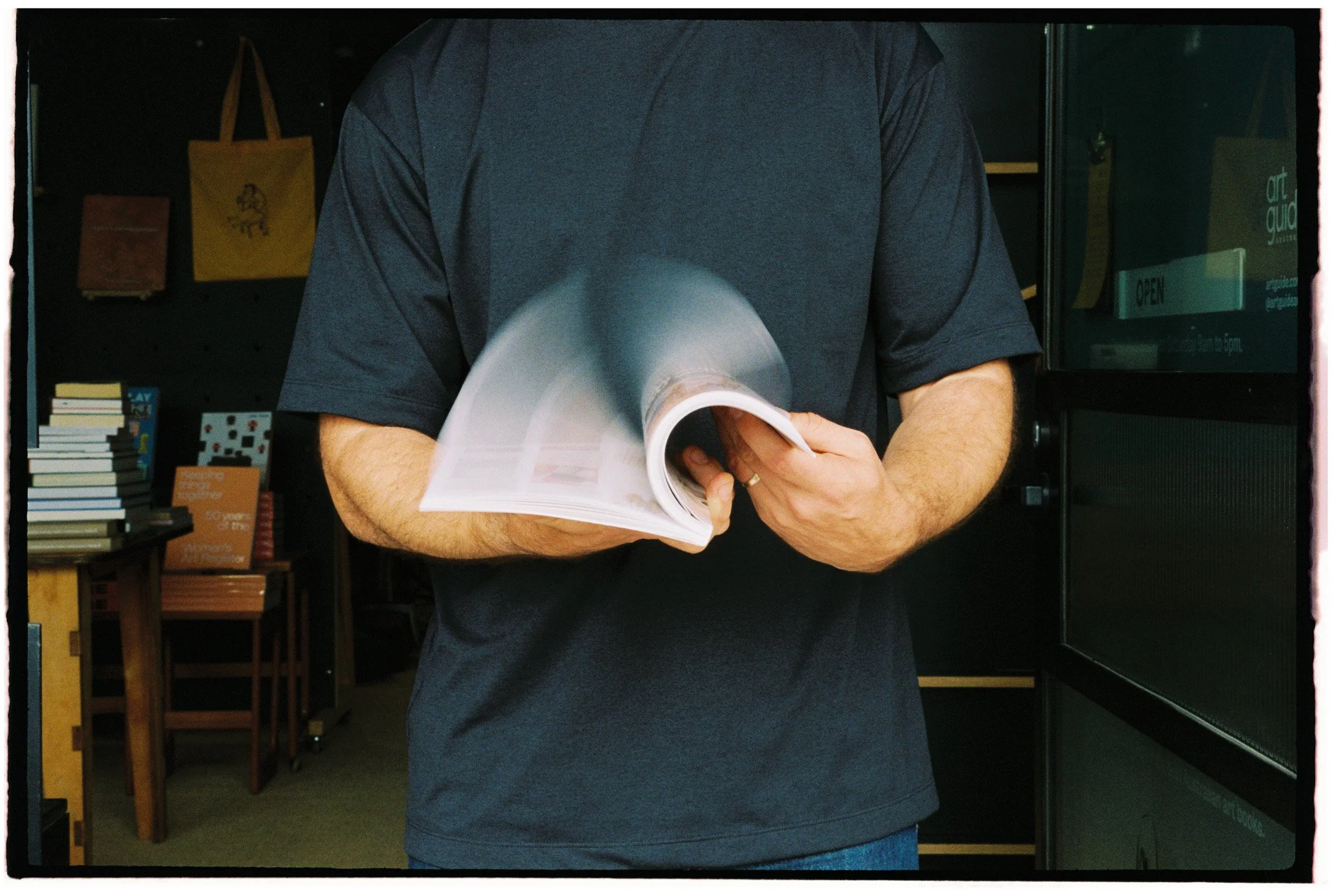 Documentary-style portrait detail of a bookseller holding an open book inside an independent bookstore.