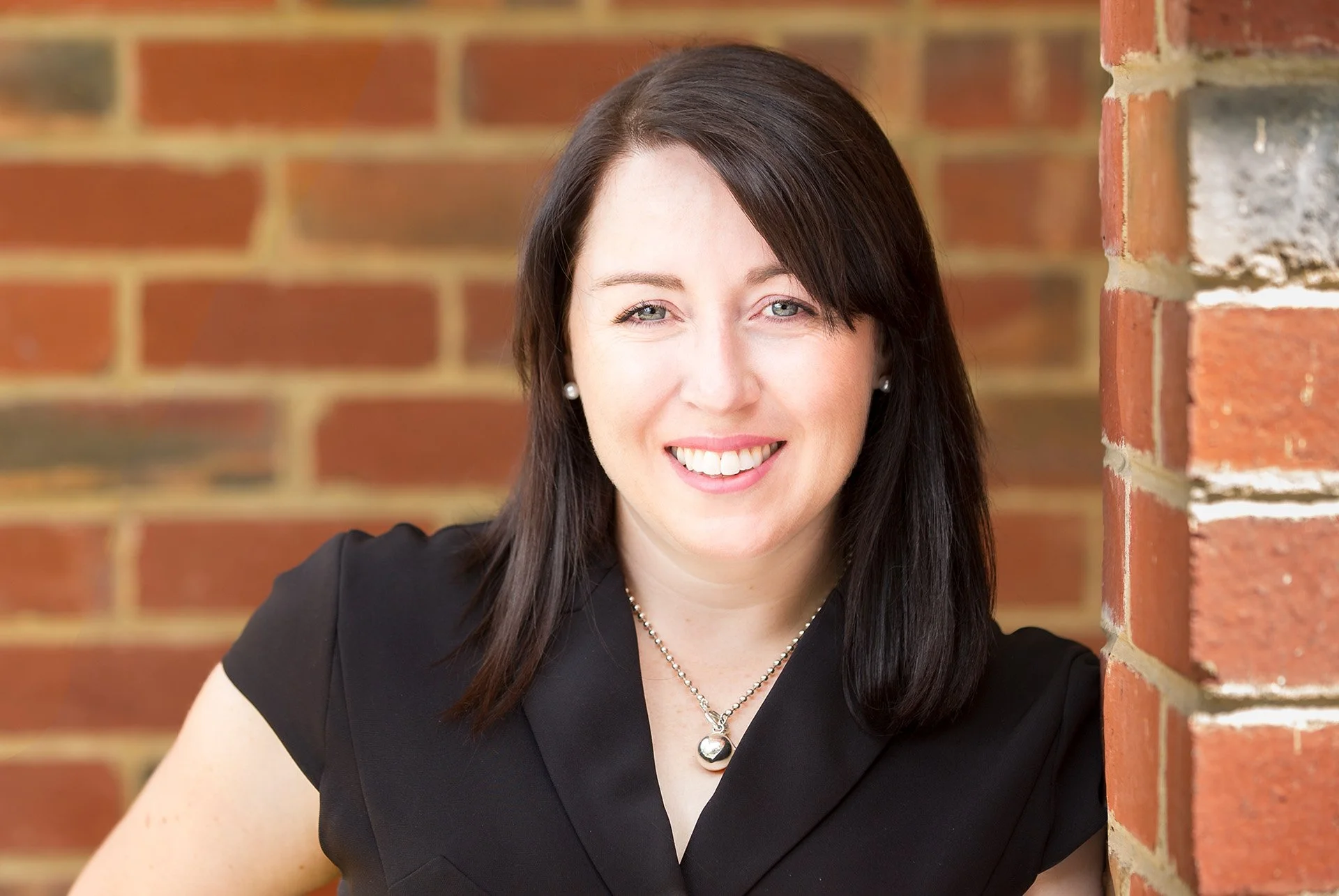 Urban feel headshot portrait of a young woman with brick wall background by Natalie Finney Photography