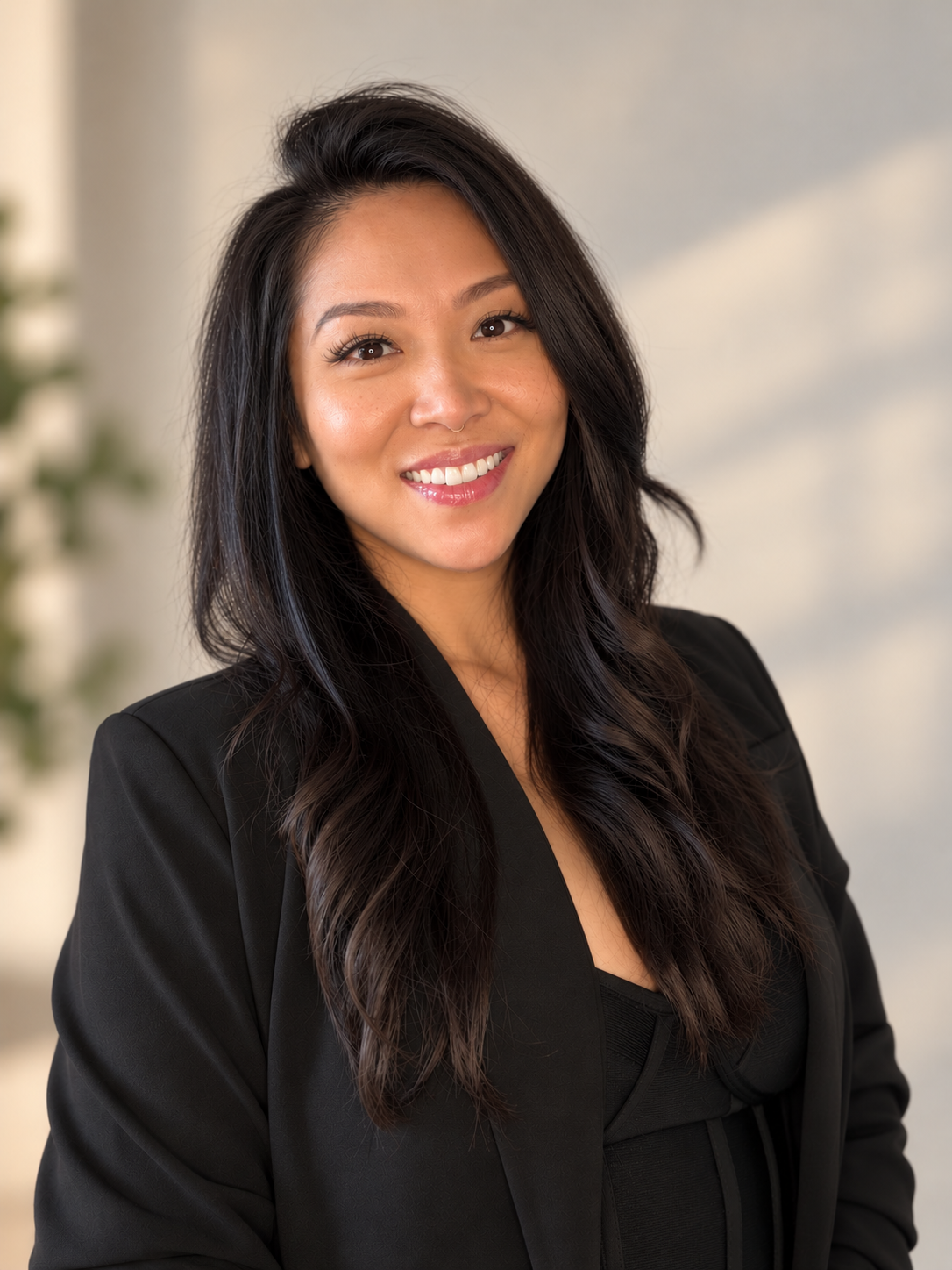 A woman with long, wavy black hair smiling and wearing a black blazer.