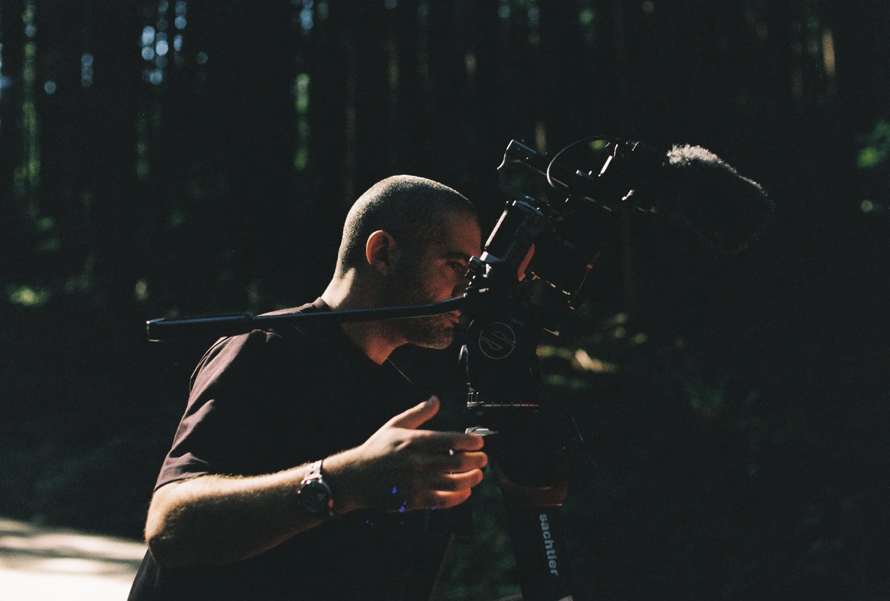 Behind the scenes: filmmaker operating a camera rig in the forest, photographed on Nikomat film.