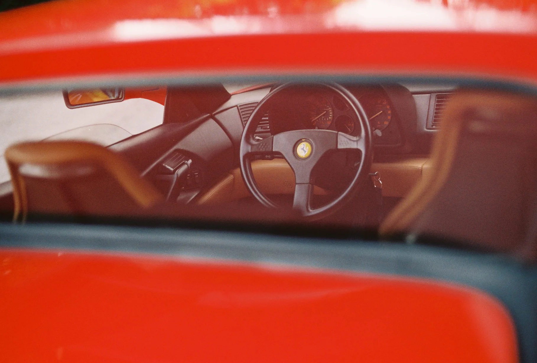 Ferrari 348 steering wheel and tan cabin seen through the side window in a Nikomat film photograph.