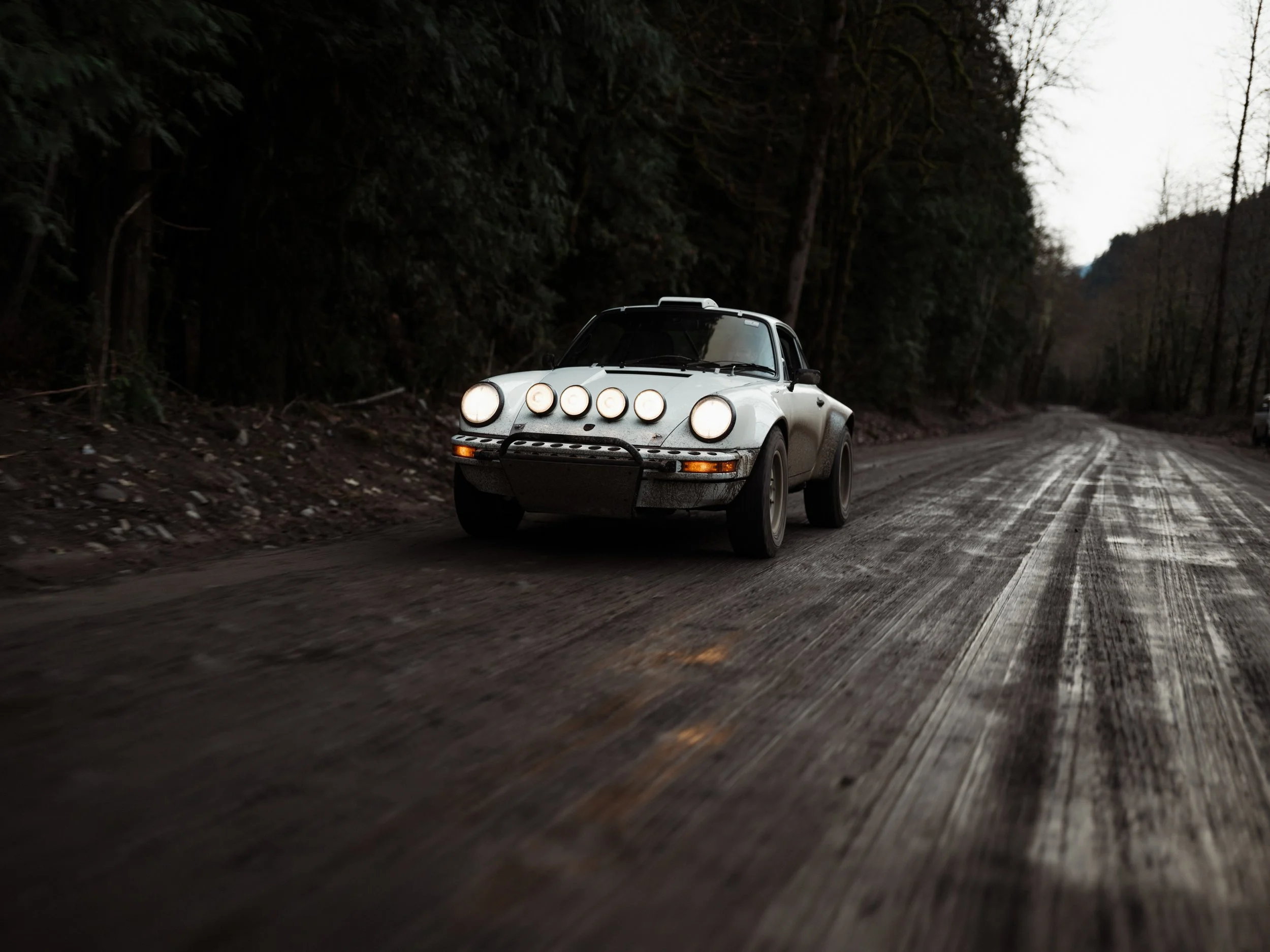 Safari Porsche 911 driving on a forest road, headlights on during an early morning photoshoot