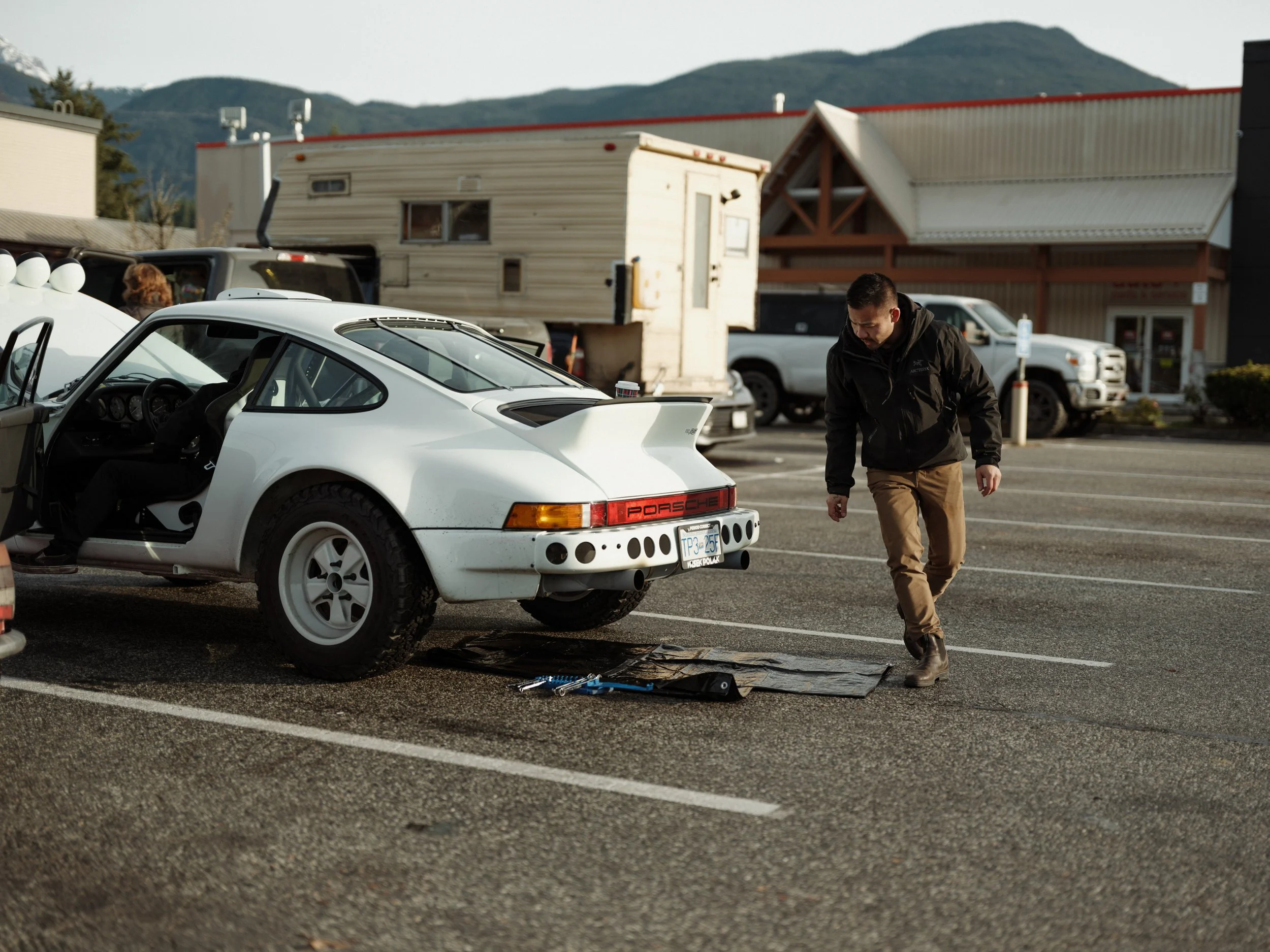 Safari Porsche 911 parked in a lot with Ryan inspecting tools and preparing for maintenance.