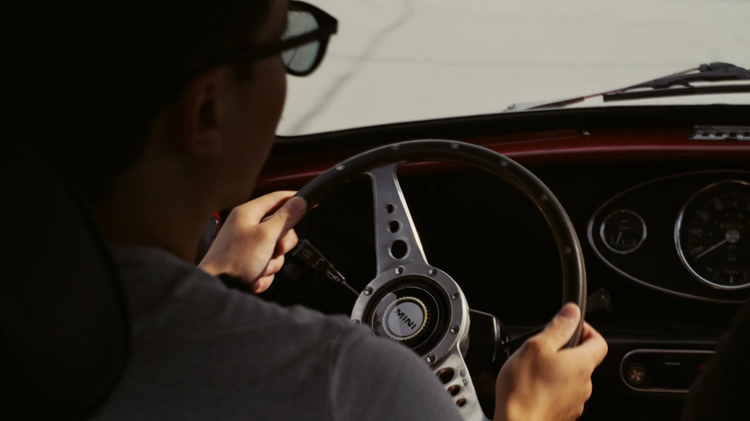 Video frame of Julian driving his classic Mini, viewed over his shoulder toward the steering wheel.