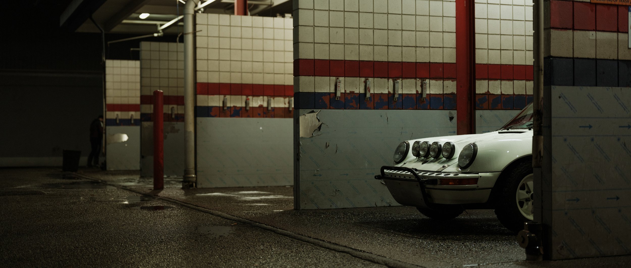 Safari Porsche 911 parked inside an empty car wash bay at night, ready for a clean after the off-road adventure.