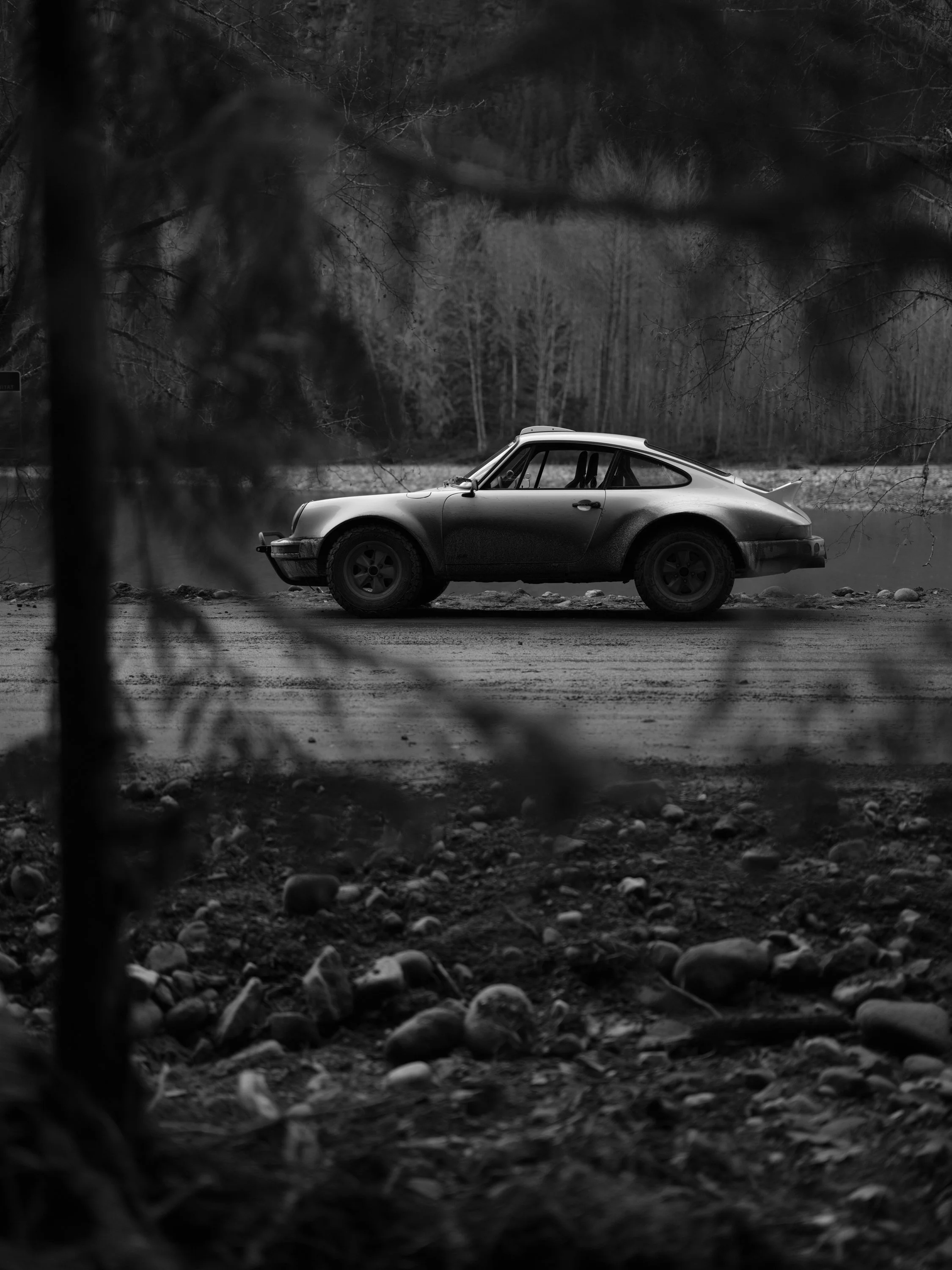 Safari Porsche 911 parked on an empty trail, photographed from behind tree branches, giving a hidden perspective.