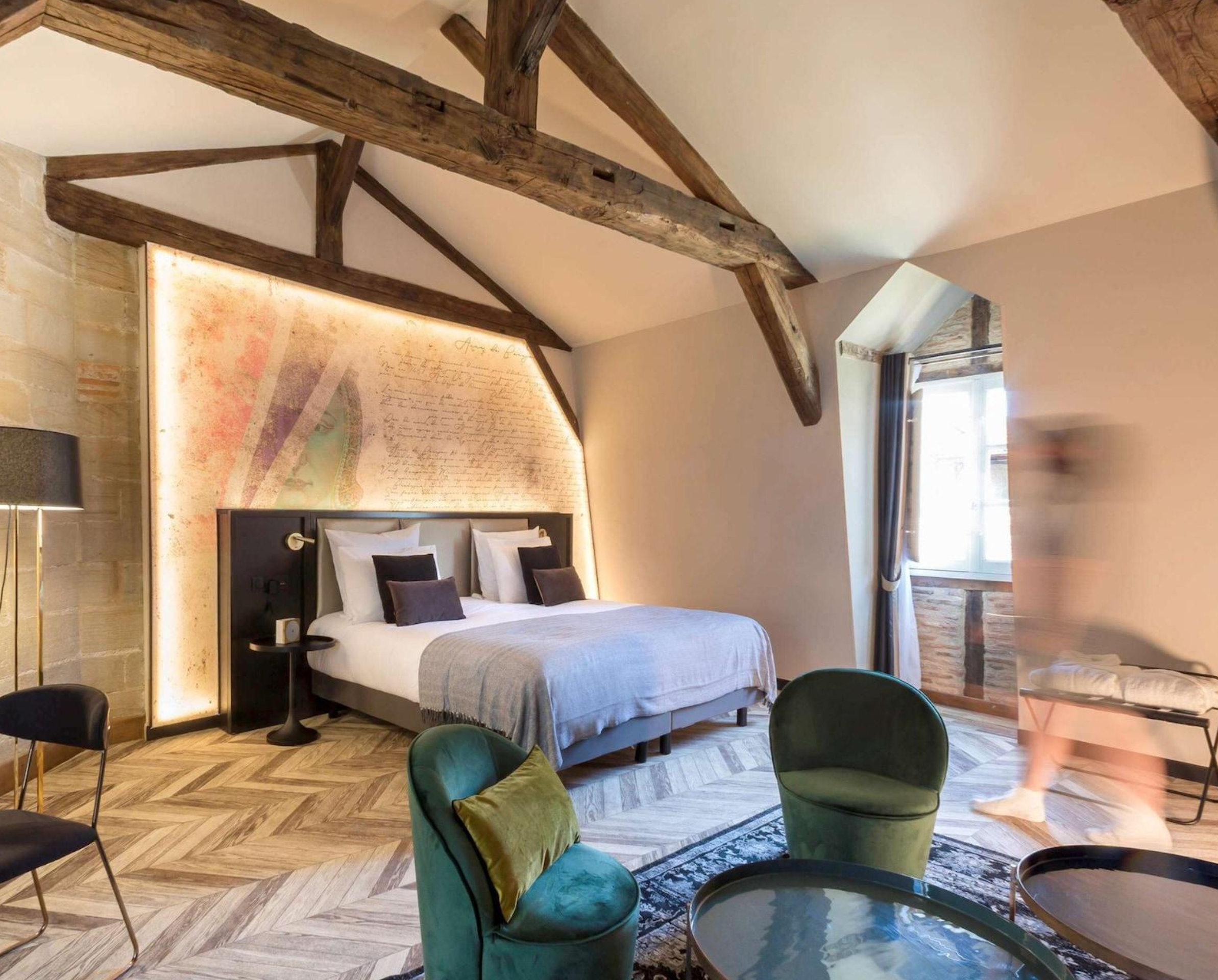 Room with a bed, green chairs, and wooden beams on the ceiling, decorated in a cozy, rustic style.