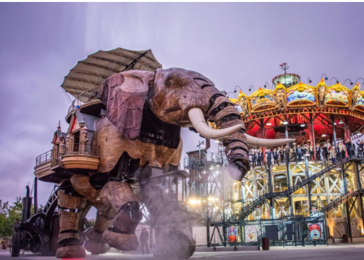 Discover Nantes - Large elephant-shaped amusement park ride with a carousel above it, with people riding and walking around.