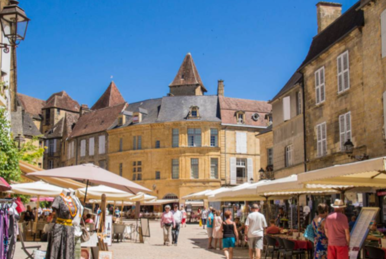 Dordogne discoveries - Sarlat outdoor market stalls in a historic town square with medieval-style buildings and clear blue sky.