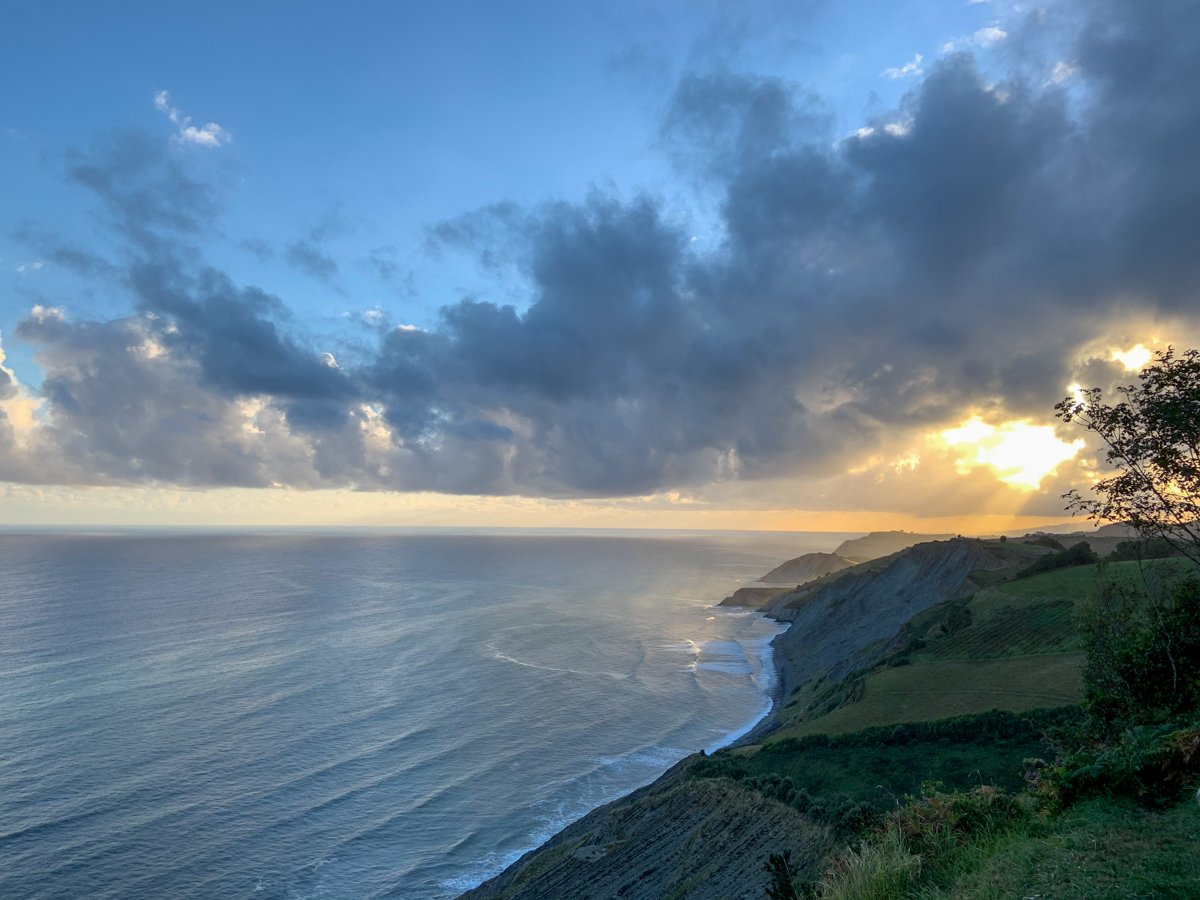Basque country - Sunset over a coastline with cliffs, showing a partly cloudy sky and the ocean.