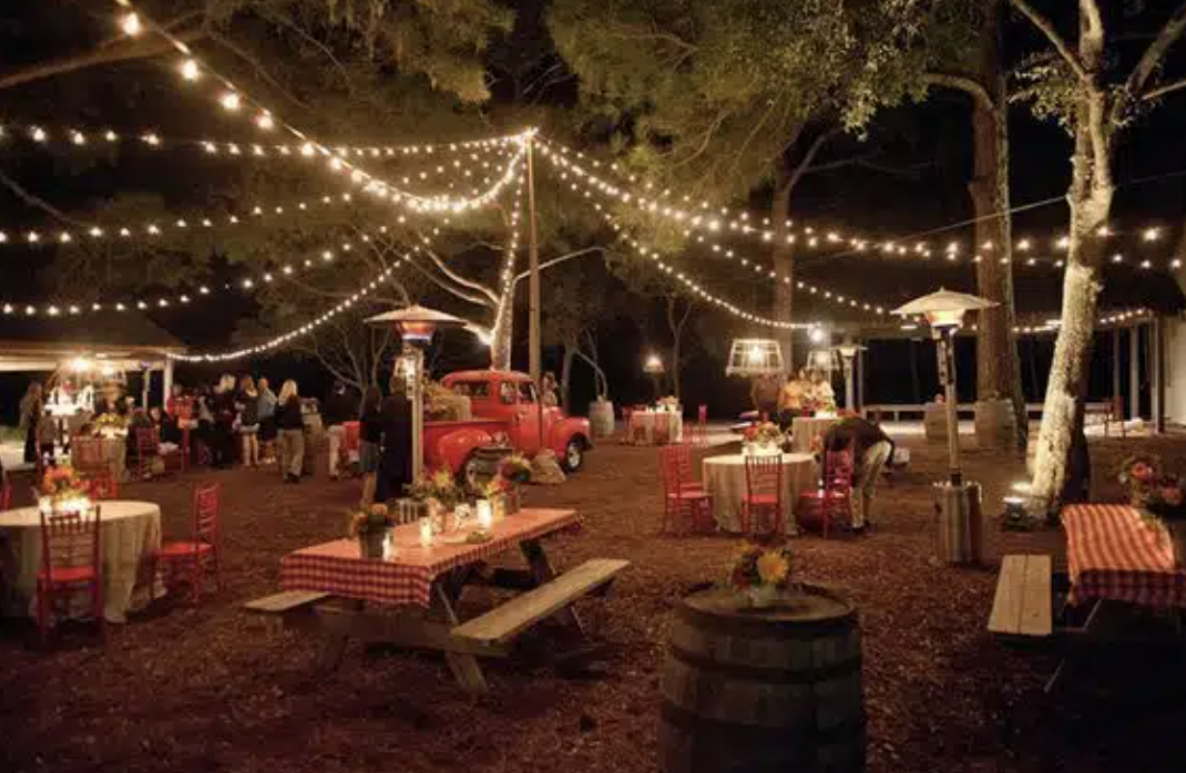 Perfect outdoor French cafes. An outdoor cafe scene in front of a gray building with the sign 'Auberge de Banne'. The cafe has red chairs and tables set with glassware and tablecloths, surrounded by green plants and flowers.