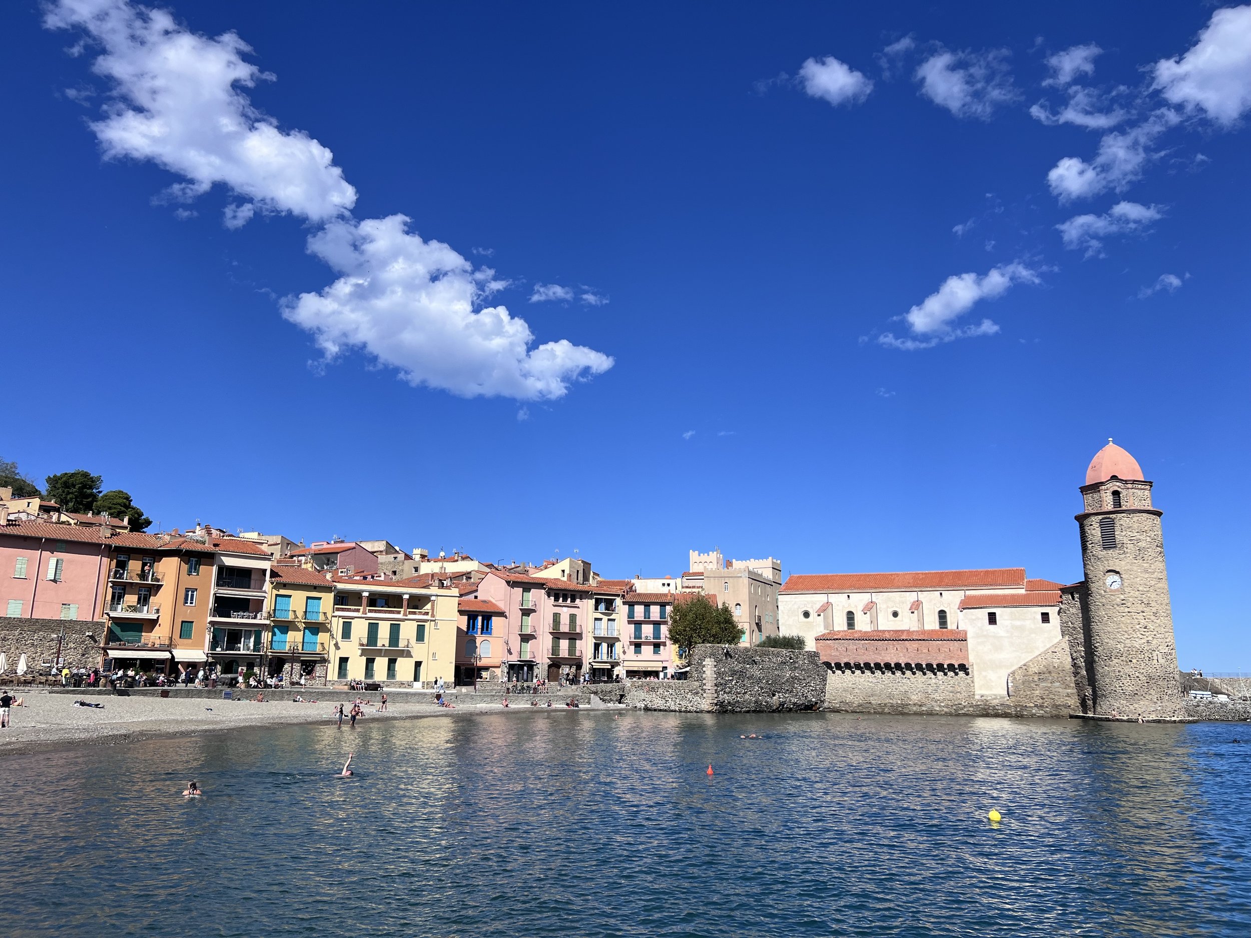 Collioure - a beautiful seaside village on the Mediterranean coast. Colorful buildings along the waterfront with a stone tower and a church against a blue sky with clouds.