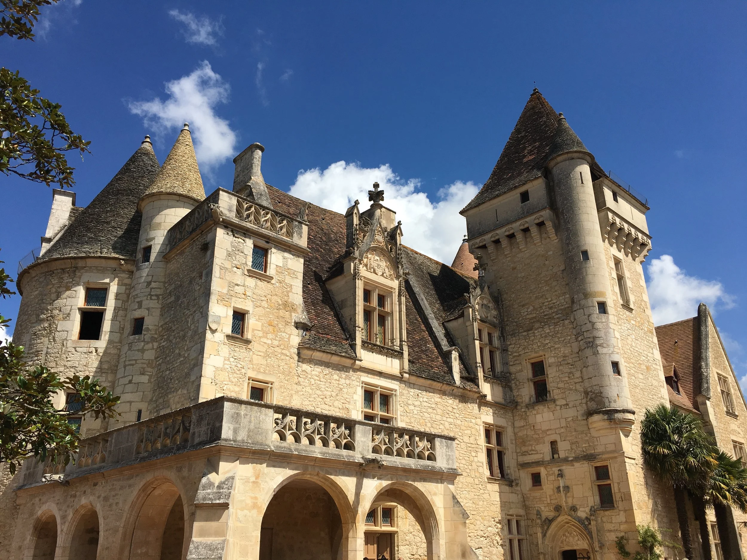 Medieval castle with stone walls, turrets, and towers under a bright blue sky with clouds.
