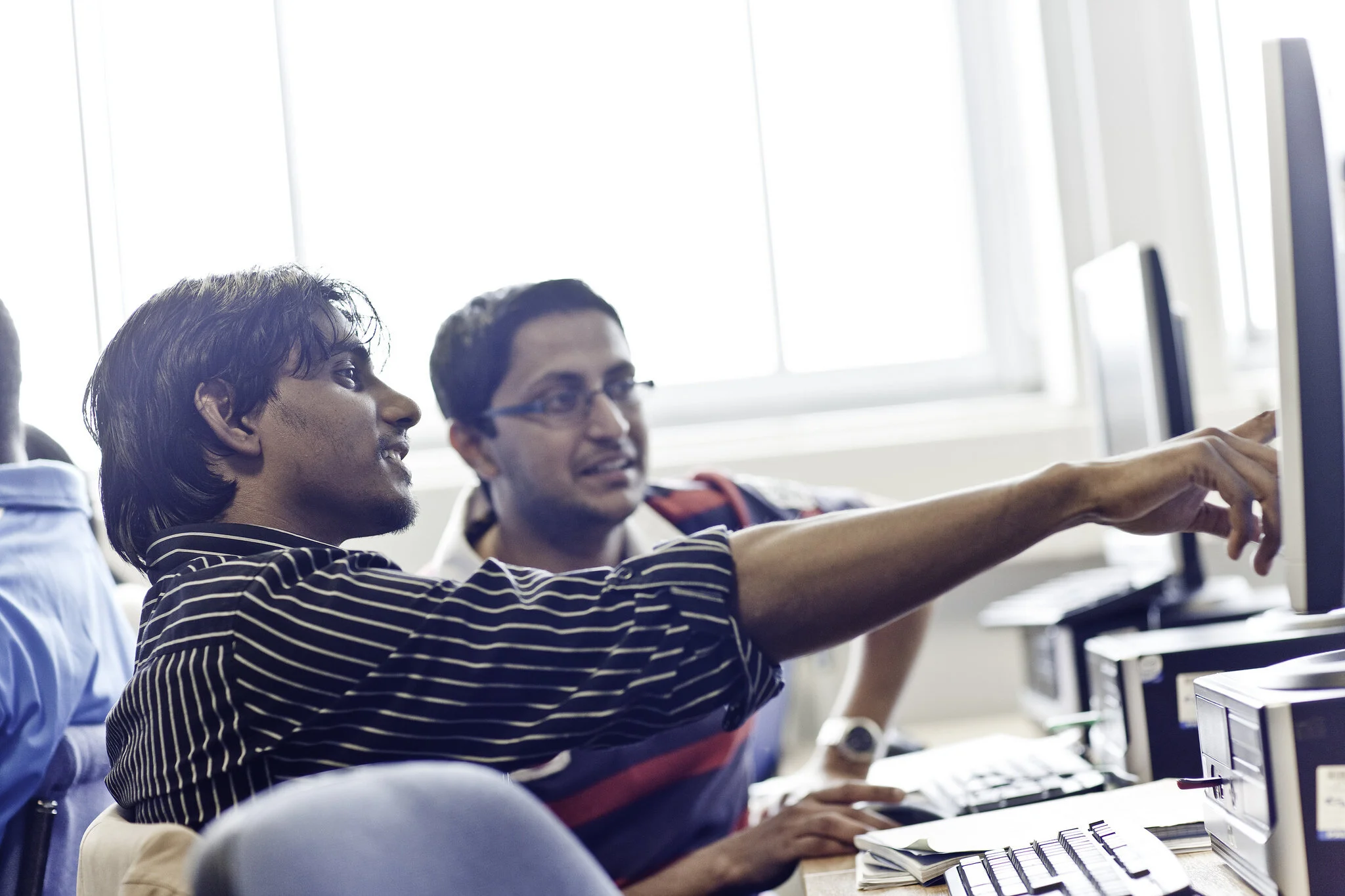 Two students in conversation whilst working together on the computer screen.