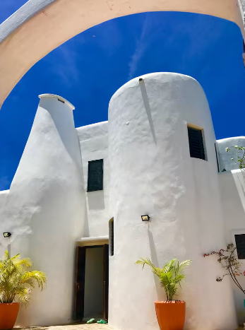 White modern building with rounded walls under a bright blue sky, potted plants at the entrance.