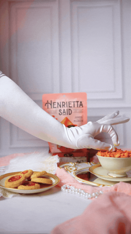 A gloved hand reaching in frame and grabbing a peanut out of a teacup surrounded by a victorian-era setup.