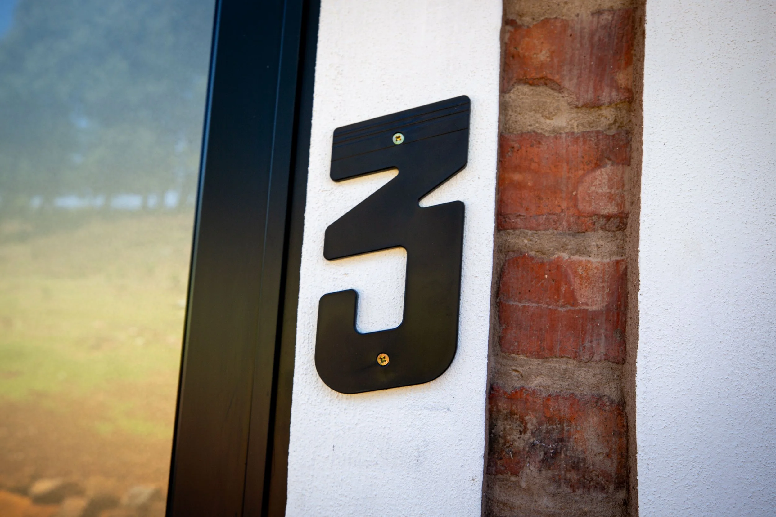House front with house number 3 in black metal numerals mounted on white wall next to a brick column.