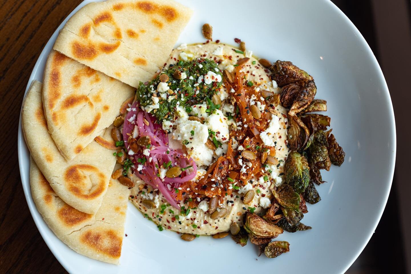 The hummus bowl has returned to our menu! Including our house made hummus, roasted brussels, zhug, harissa onion jam, pepita, pickled onion, feta, and toasty pita. Add grilled chicken for an extra boost of protein. This one is packed with fun flavors