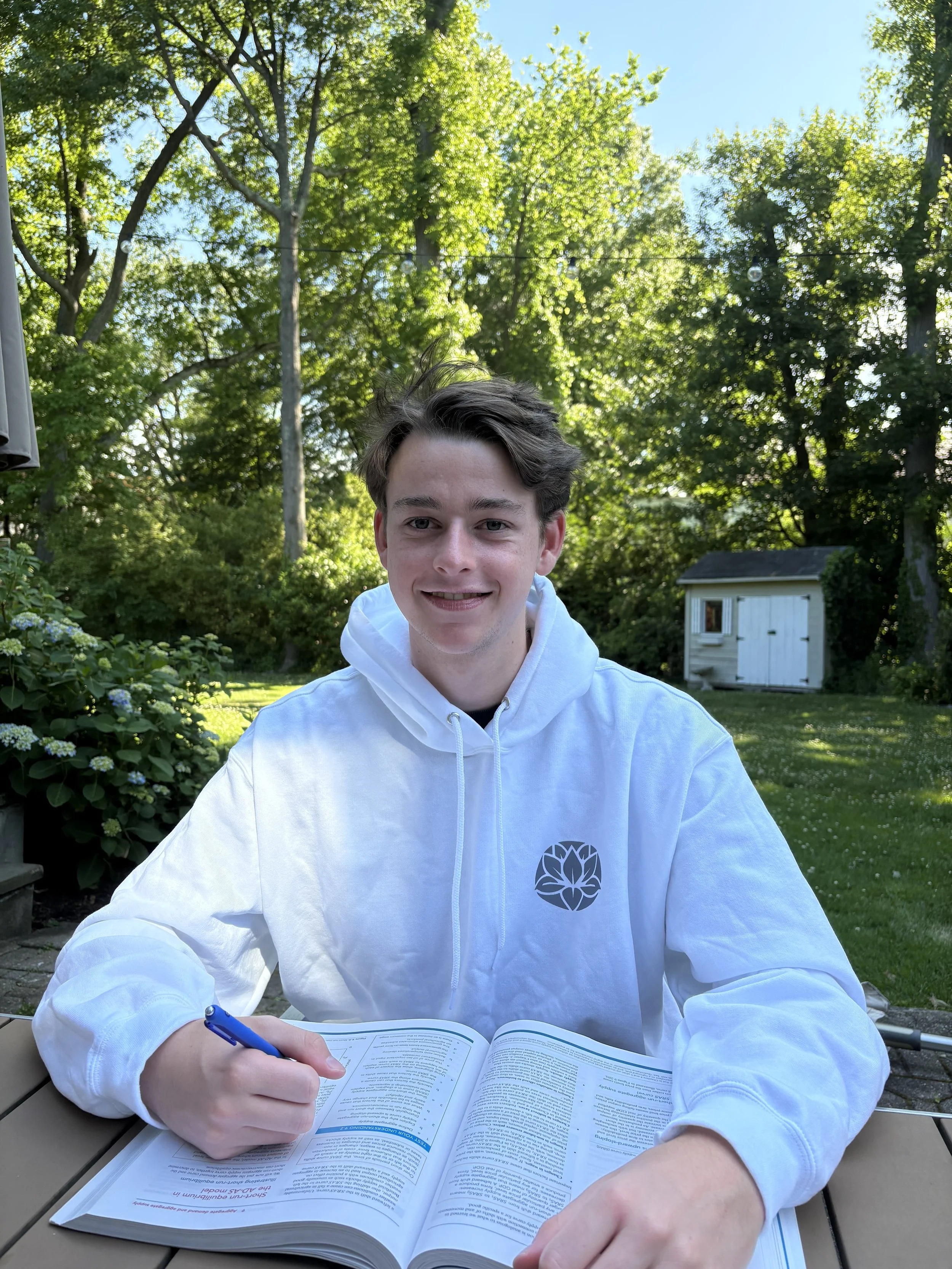 Anatole Baxter of the ShareLove.Fund Youth Leadership Board sitting down wearing a white sweatshirt with a textbook open on a table.