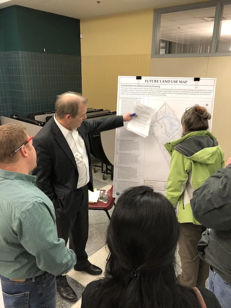 Man in suit explaining a land use map to a group of people at an indoor meeting.