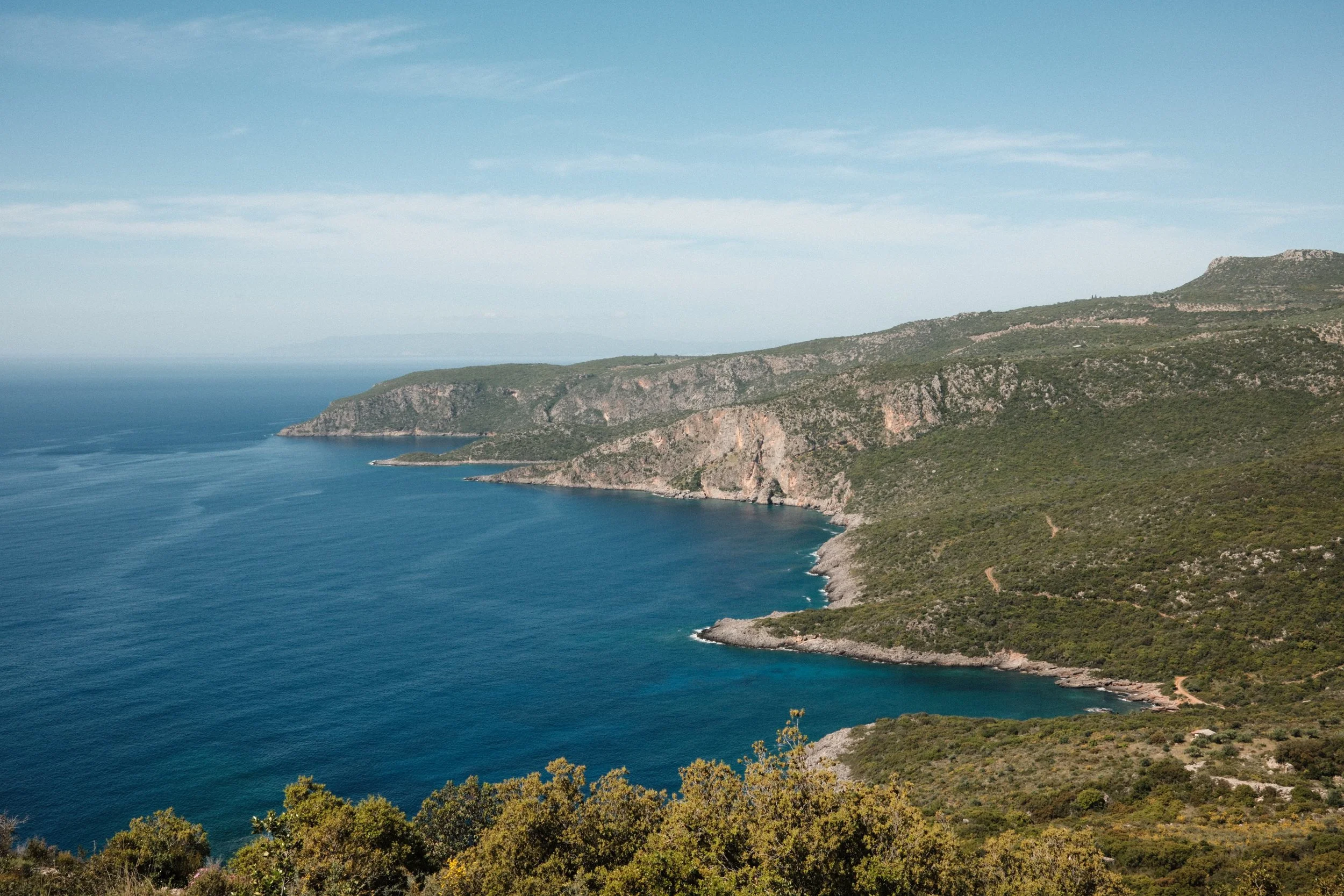 Scenic view of a rugged coastline with green hills and cliffs overlooking the blue ocean under a partly cloudy sky.