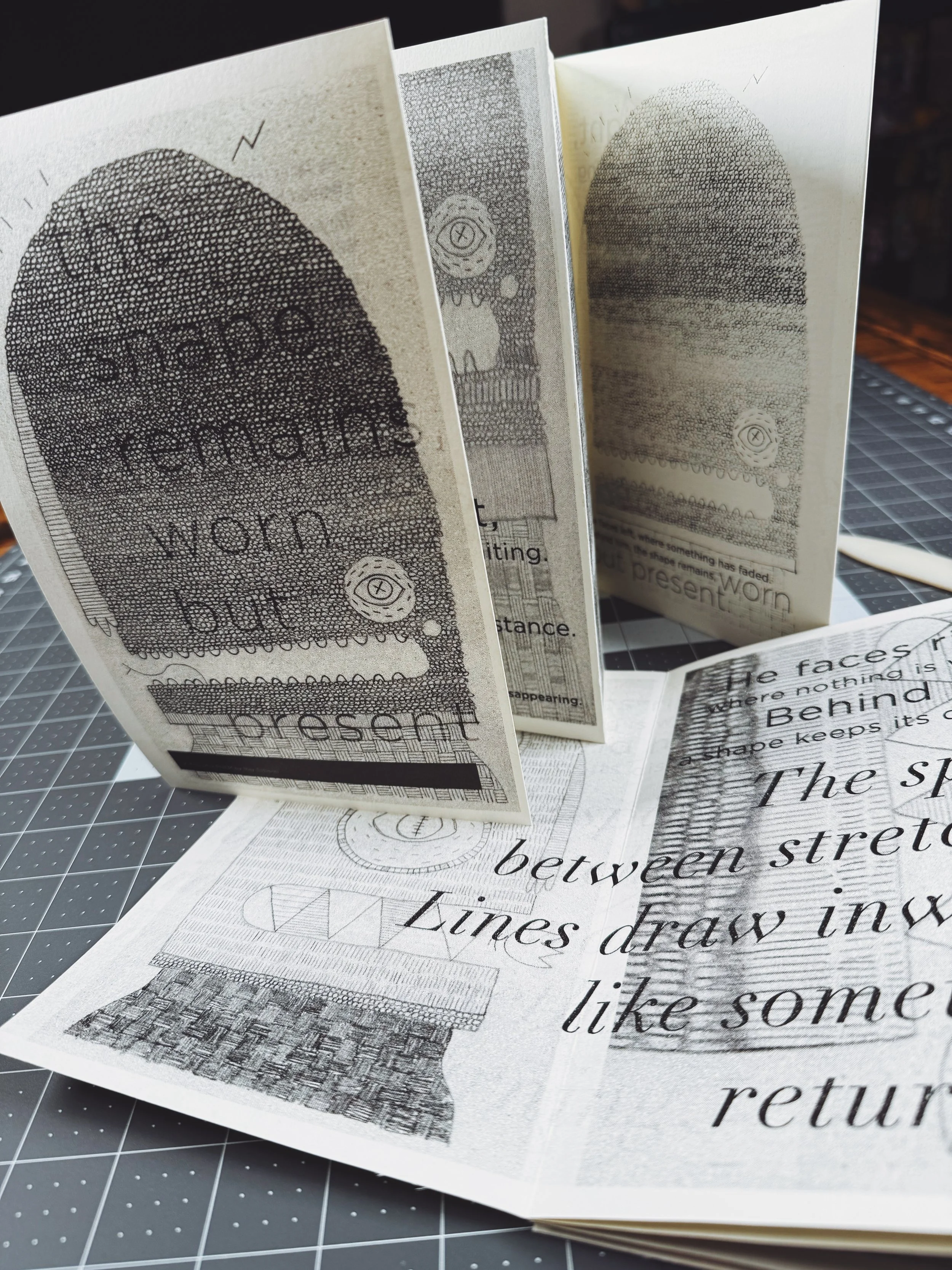 Open booklet or brochure with black-and-white illustrations and text, positioned on a cutting mat with grid lines.