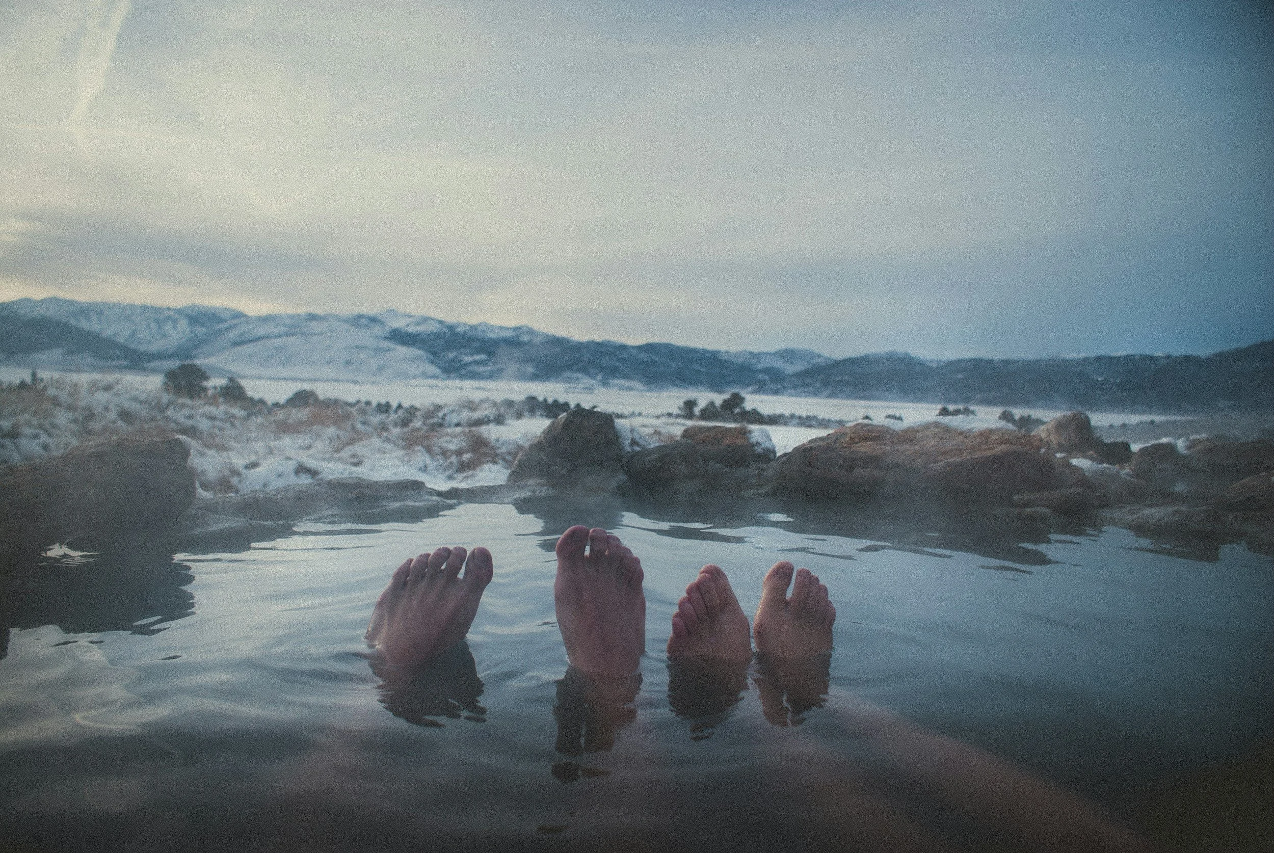 feet pointing up from the water with a mountain range in the background