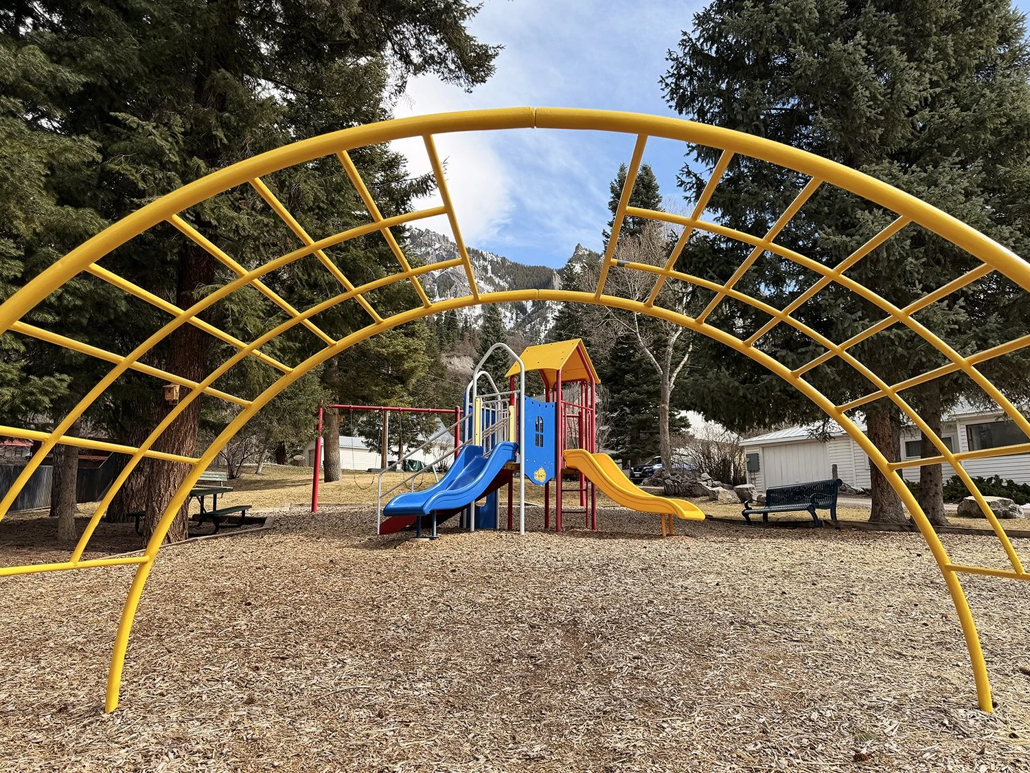 A yallow jungle gym frames a blue, yellow, and red playground.