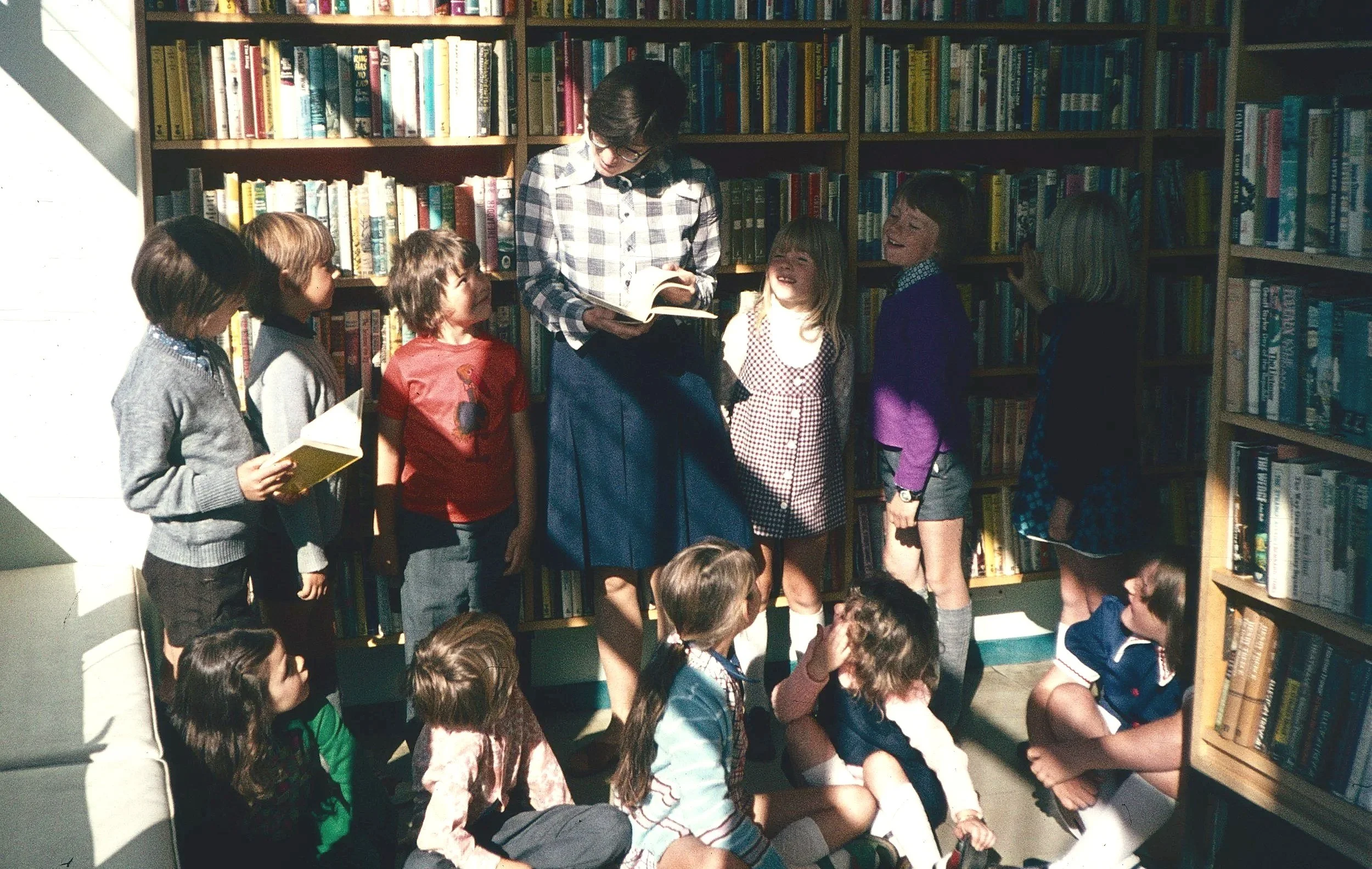 Women reading a book to kids in library
