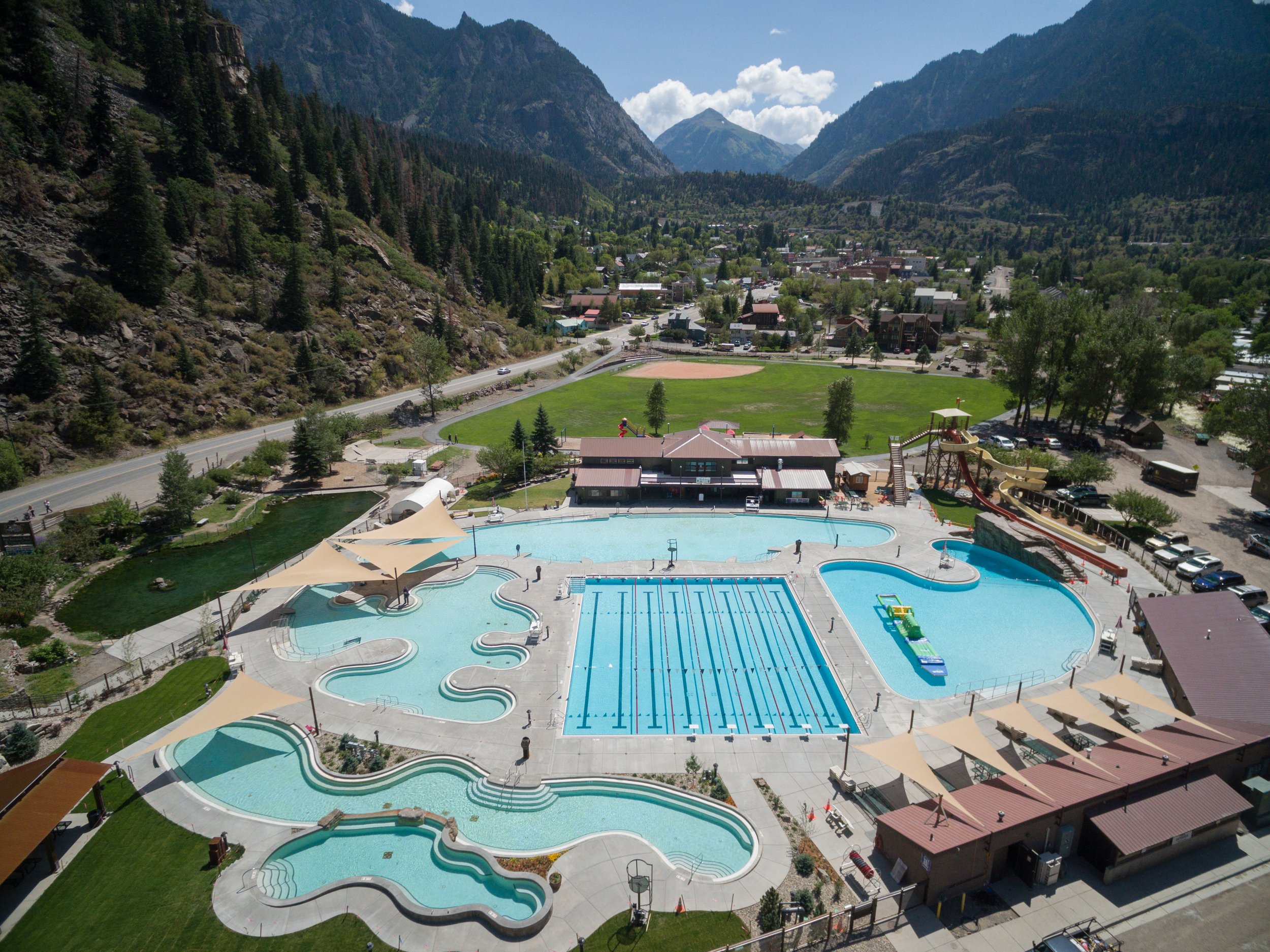 An aerial view of Ouray, Colorado, showing the Ouray Hot Springs Pool, Fellin Park, the Goldfish Pond, and Mount Abrams in the background.