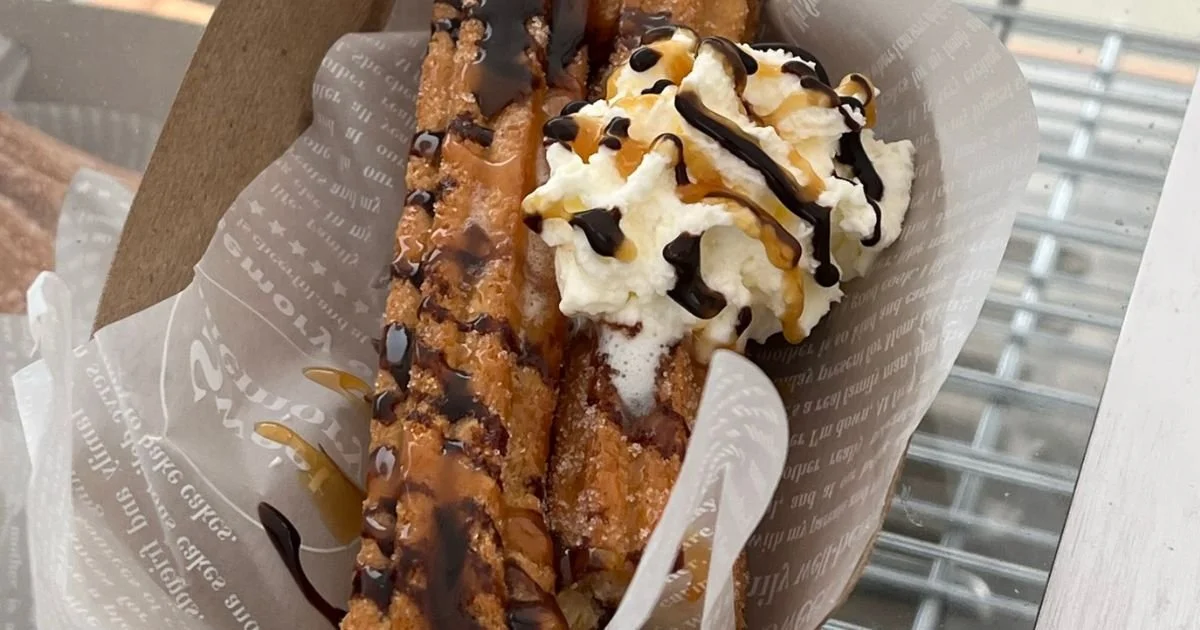 a close up of churros on a tray with chocolate drizzle and premium whipped cream