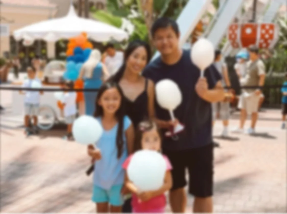A family of four, with two young girls and their parents, standing at an outdoor event holding white cotton candy.