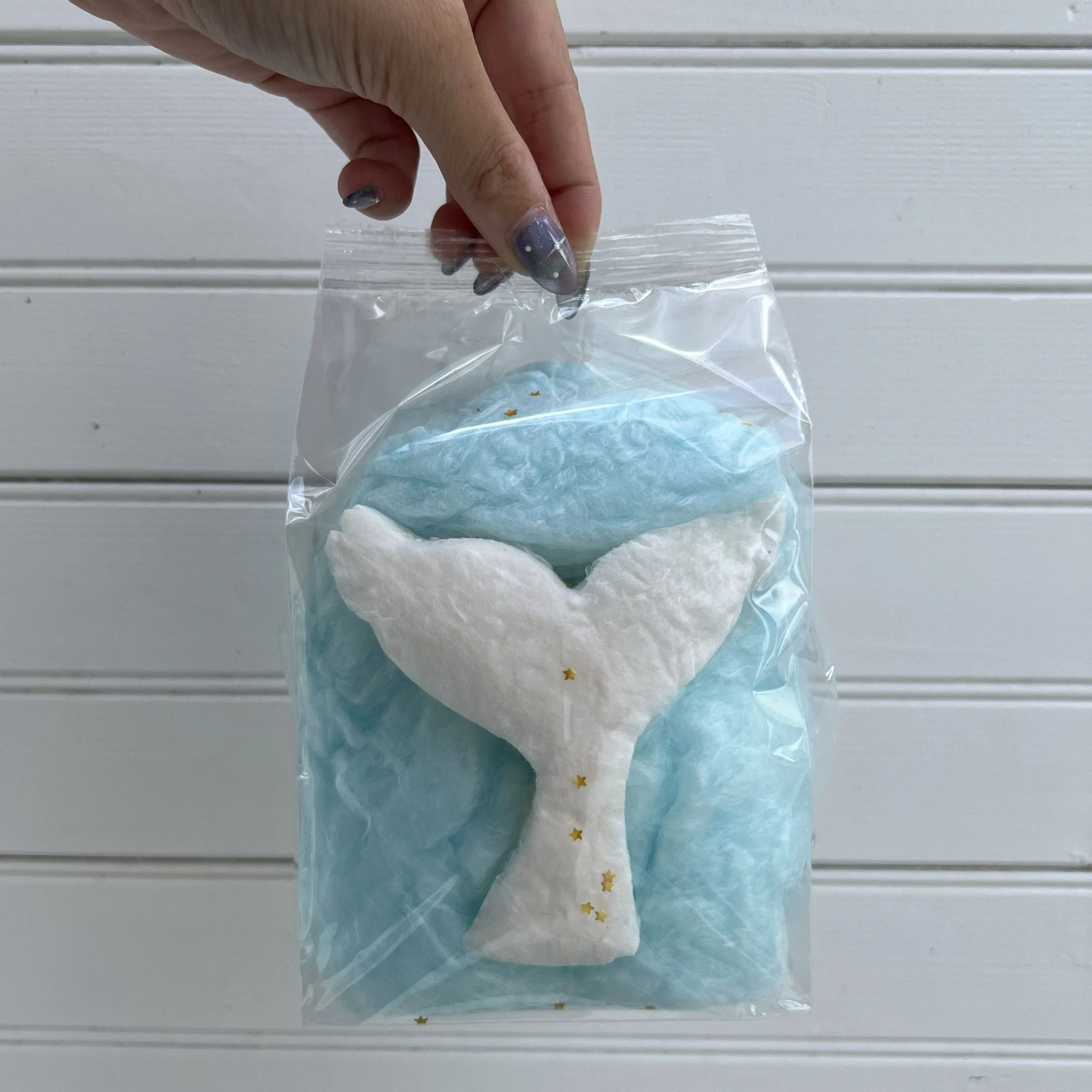 a hand holding up a cotton candy favor bag with an edible mermaid tail shape in the bag.
