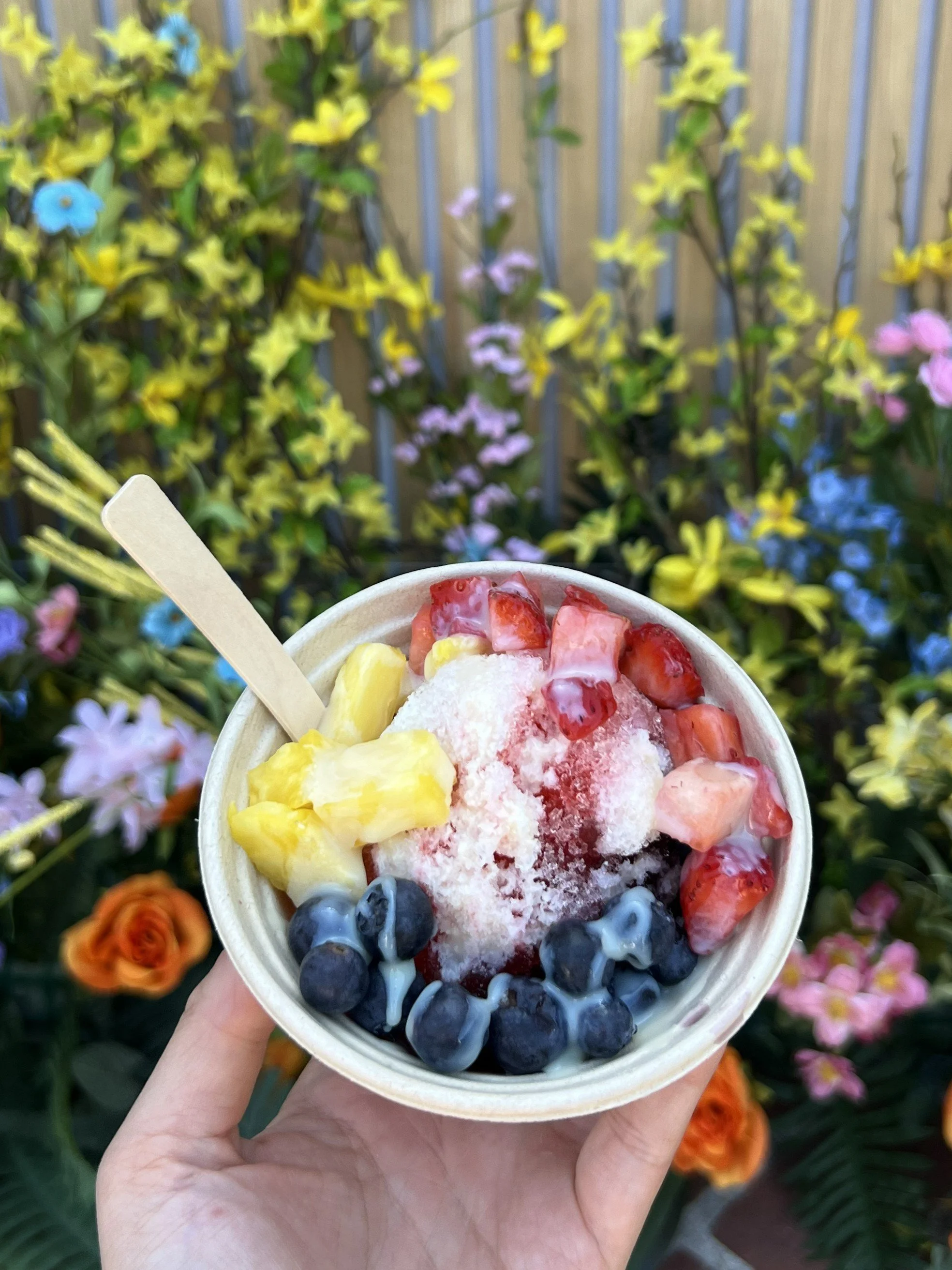 a bowl of the jolly sheep shaved ice with fresh cut fruit and sweet condensed milk held against a backdrop of flowers