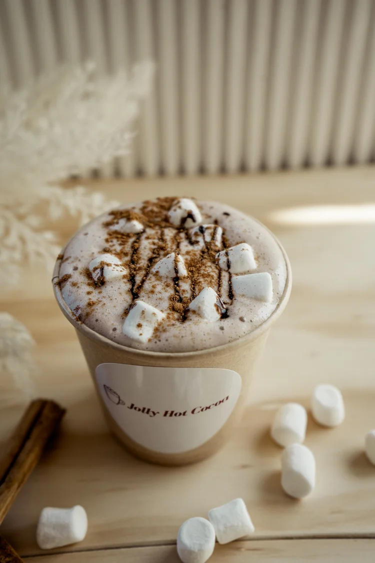 A cup of Jolly Sheep hot chocolate topped with marshmallows, cinnamon powder and chocolate drizzle.