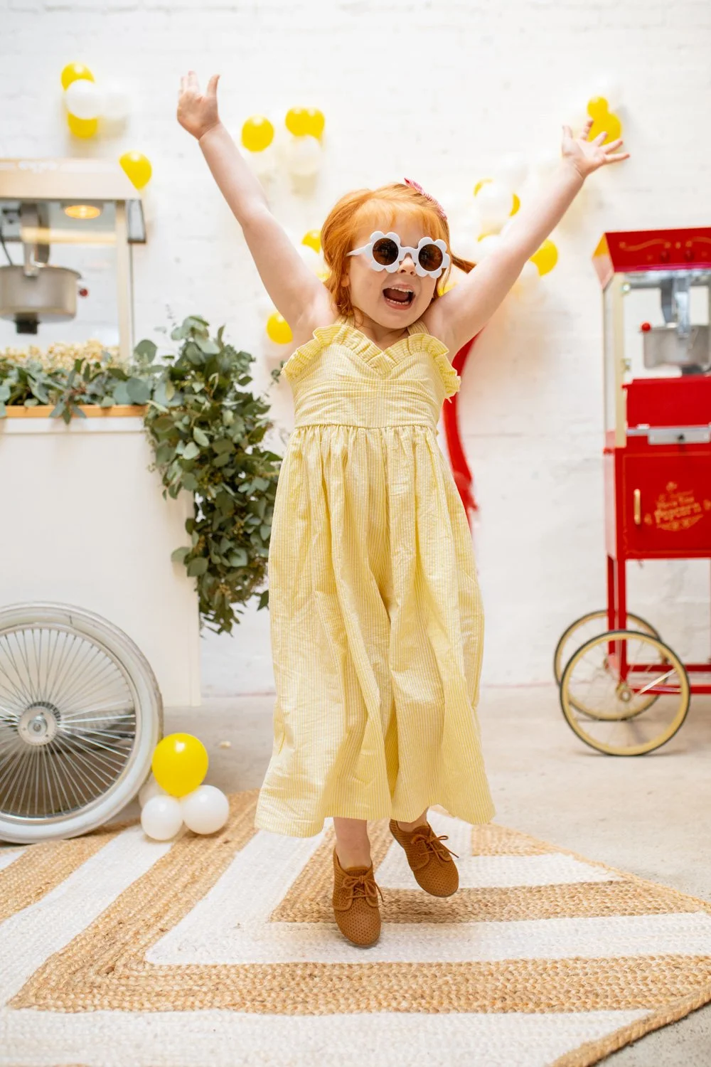 Little girl with cool glasses jumping for joy in front of a modern popcorn cart on the left and a classic one on the right