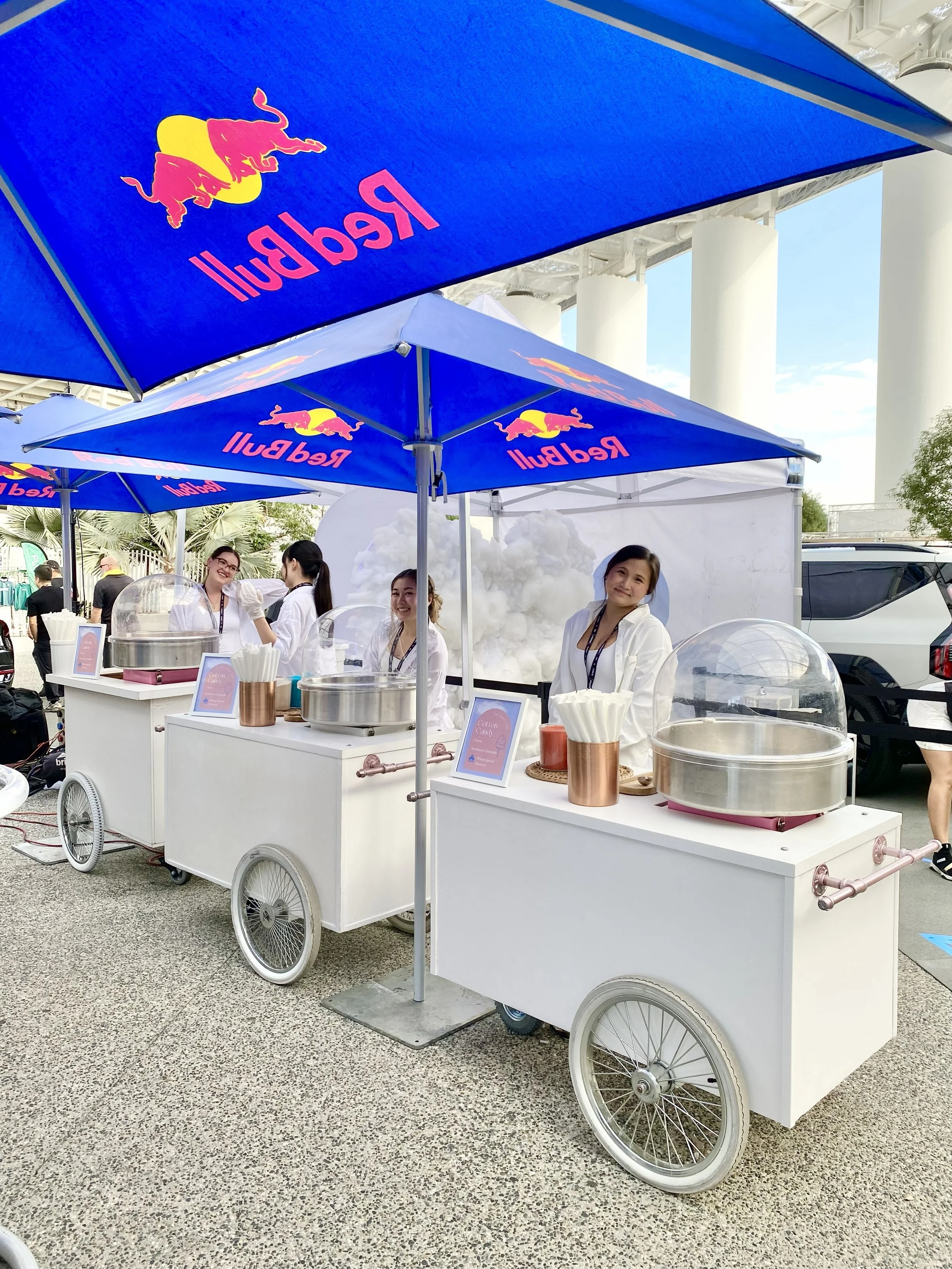 4 Jolly Sheep attendants servicing 3 cotton candy carts under Red Bull branded umbrellas at an event