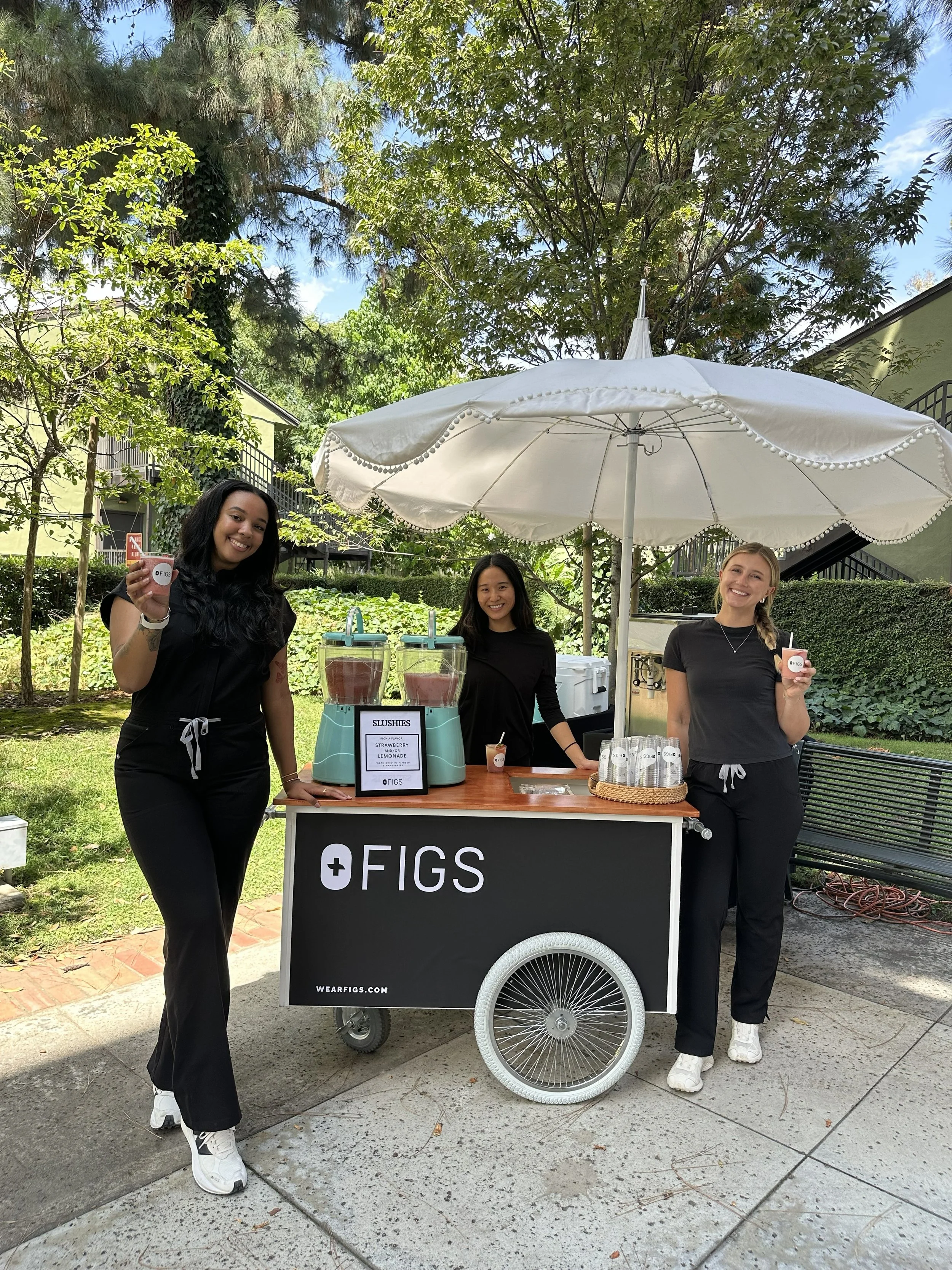 three girls standing around a slushy cart at a FIGS branded event