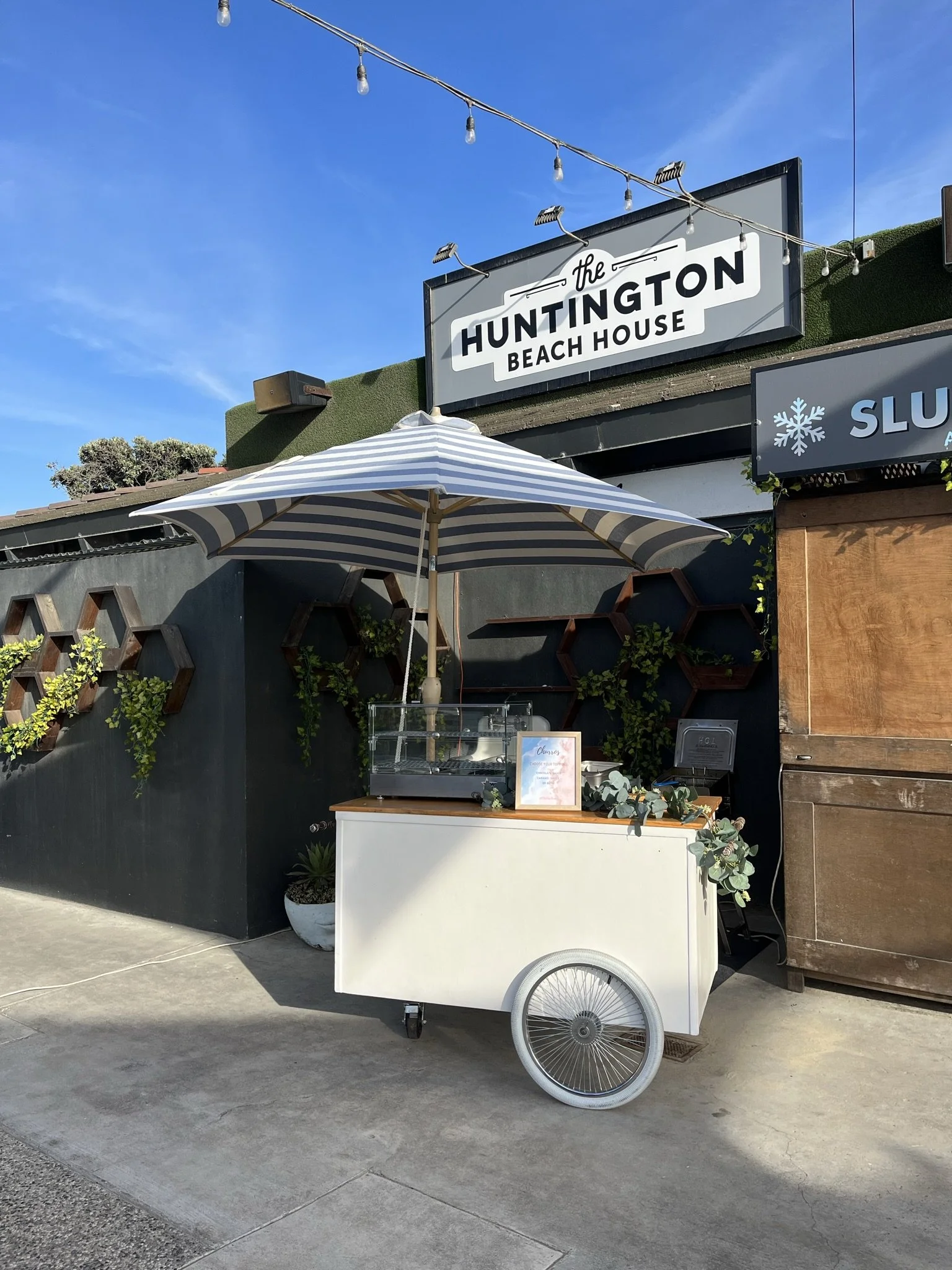 the jolly sheep churro cart with striped umbrella set up at huntington beach house for a corporate event